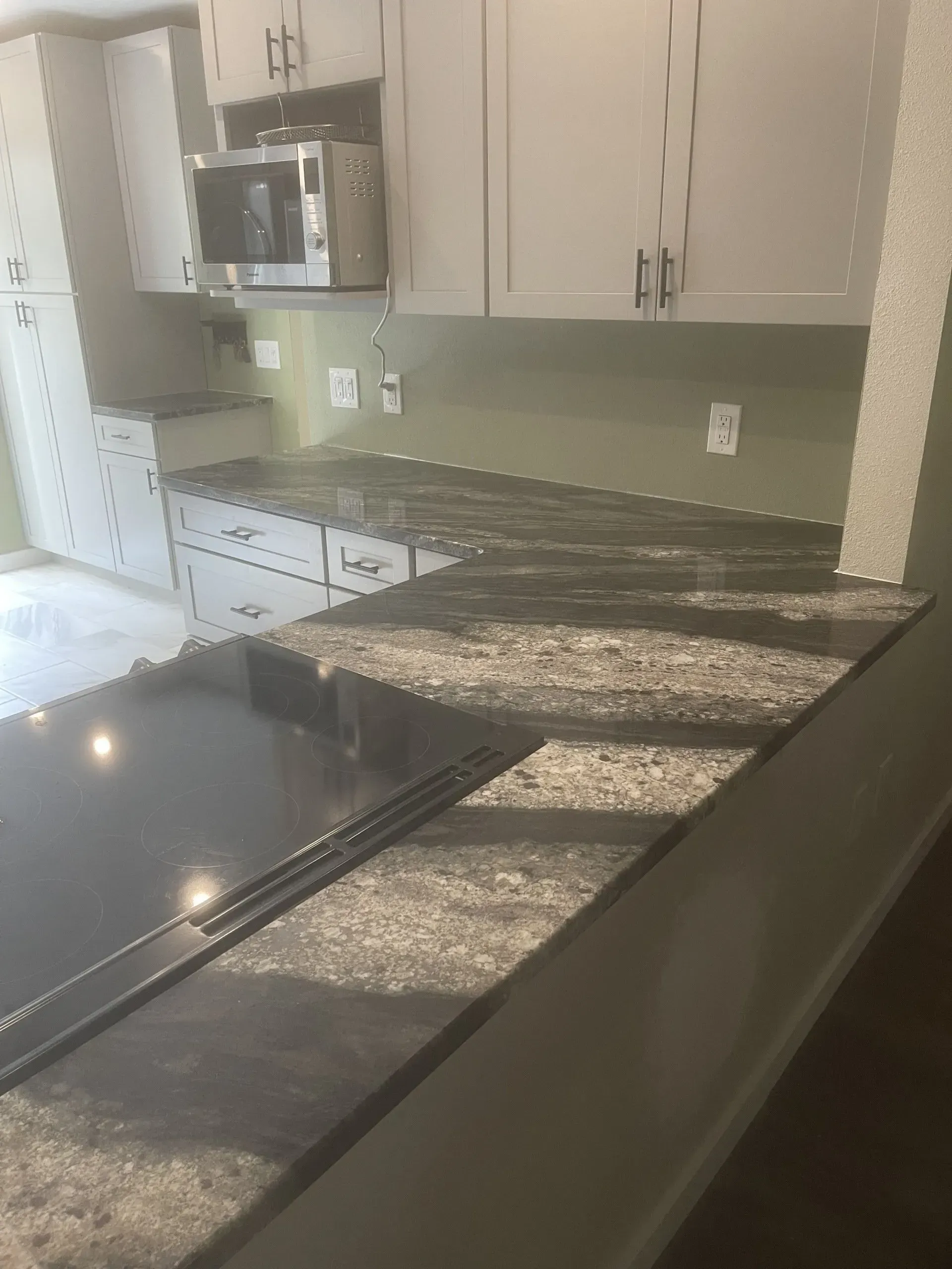 Kitchen countertop with black granite island, gray cabinets, and built-in microwave.