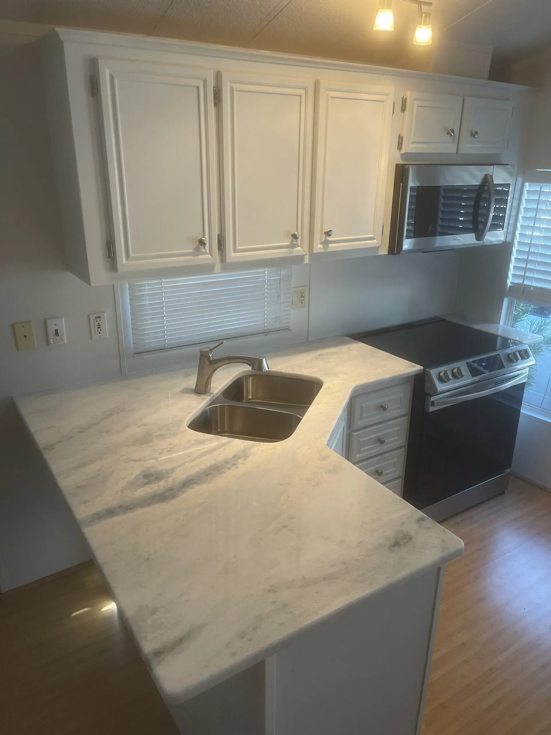 Modern kitchen with white cabinets, marble countertop, stainless sink, and black stove in warm lighting