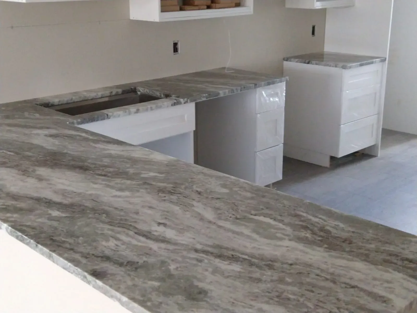 Kitchen with gray marble countertop, white cabinets, and two appliances in a remodel setting