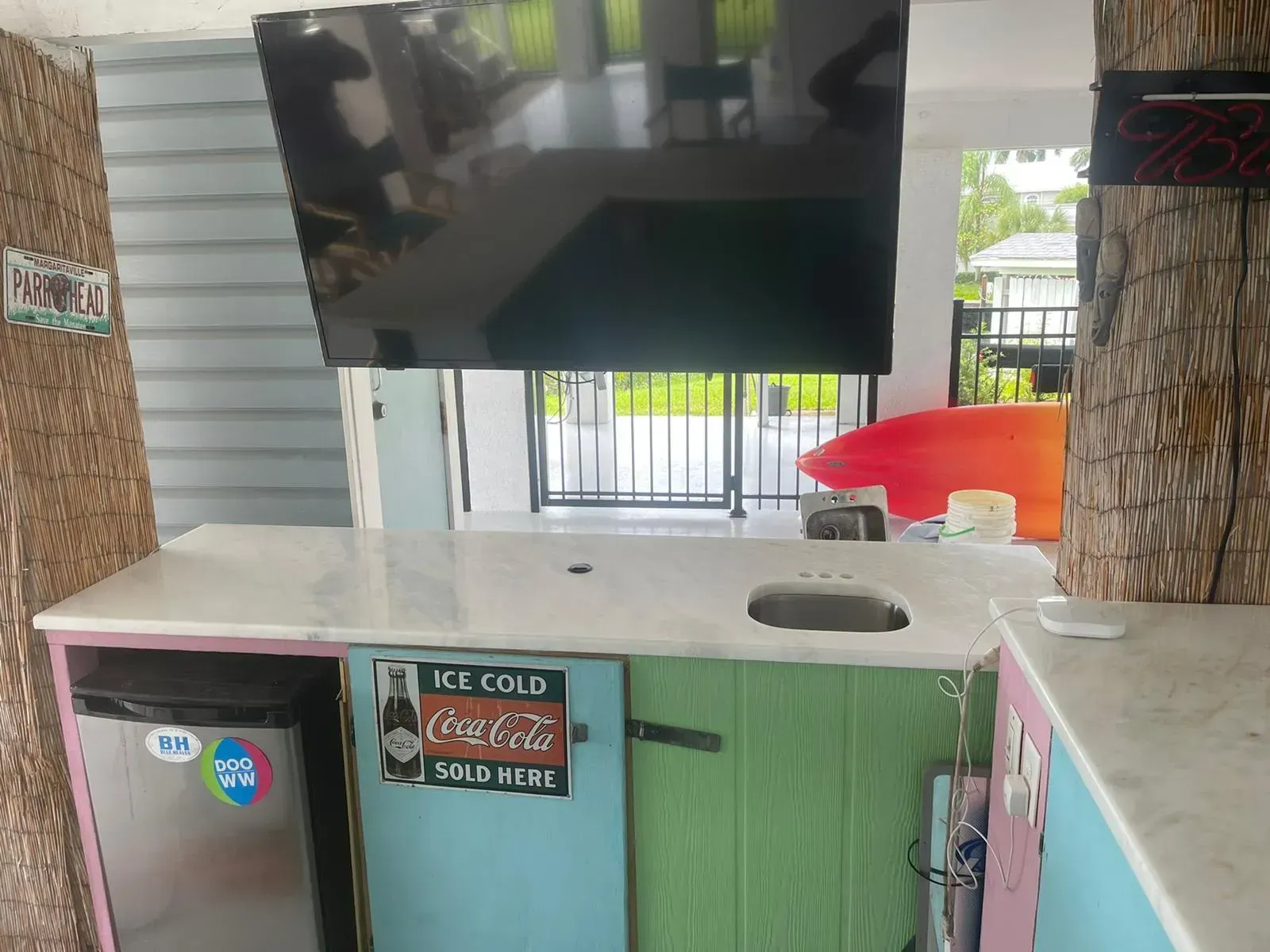 Outdoor TV mounted above a counter with a green cabinet and a small sign in a covered patio area