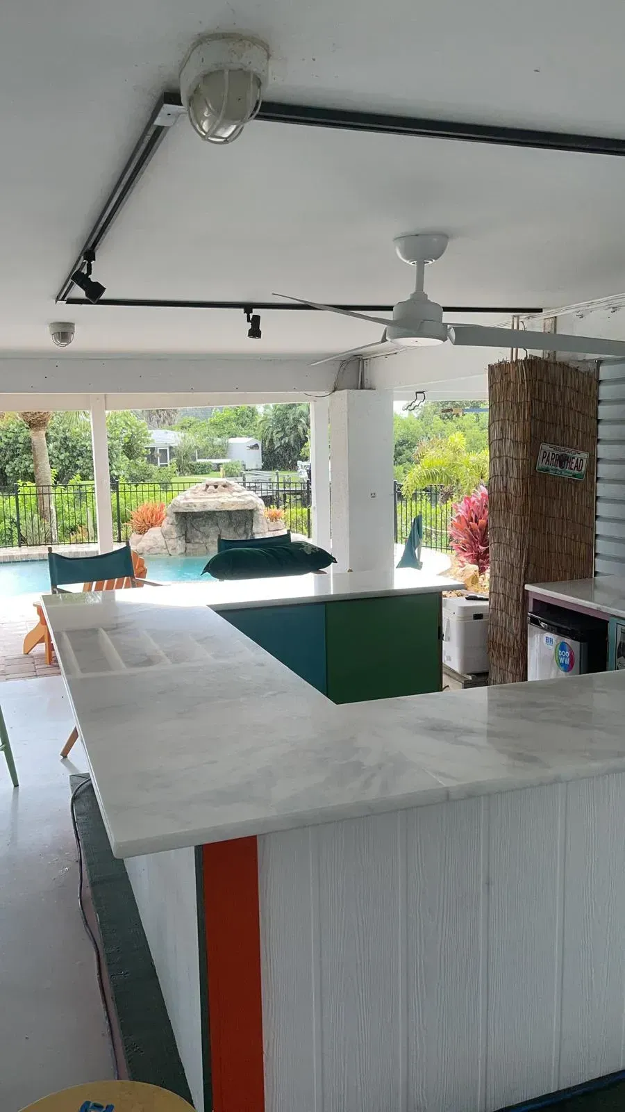 Open-air patio bar with a marble counter, ceiling fan, and poolside seating overlooking greenery