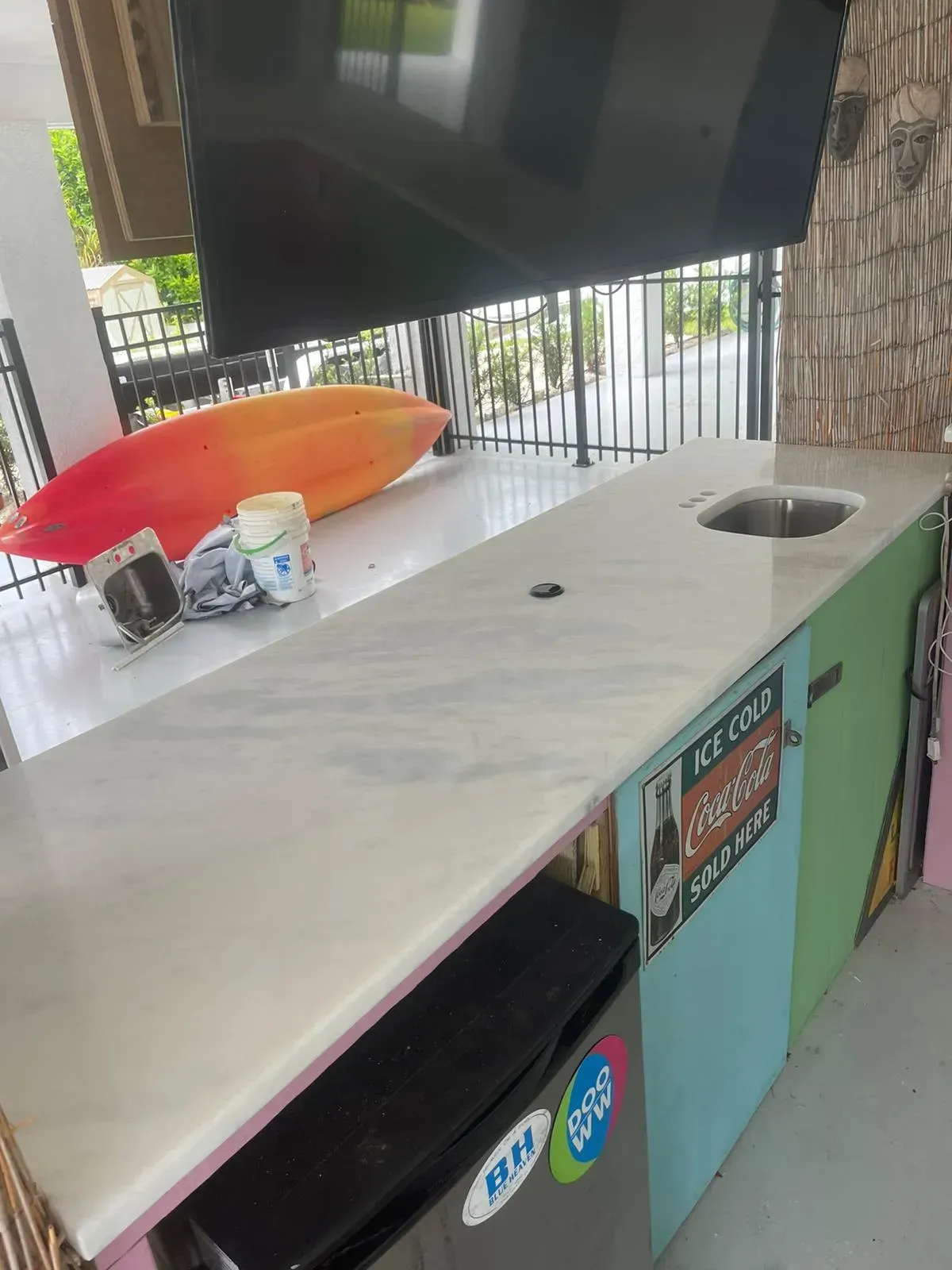 White countertop with a sink cutout on a porch, with an orange kayak and buckets nearby.