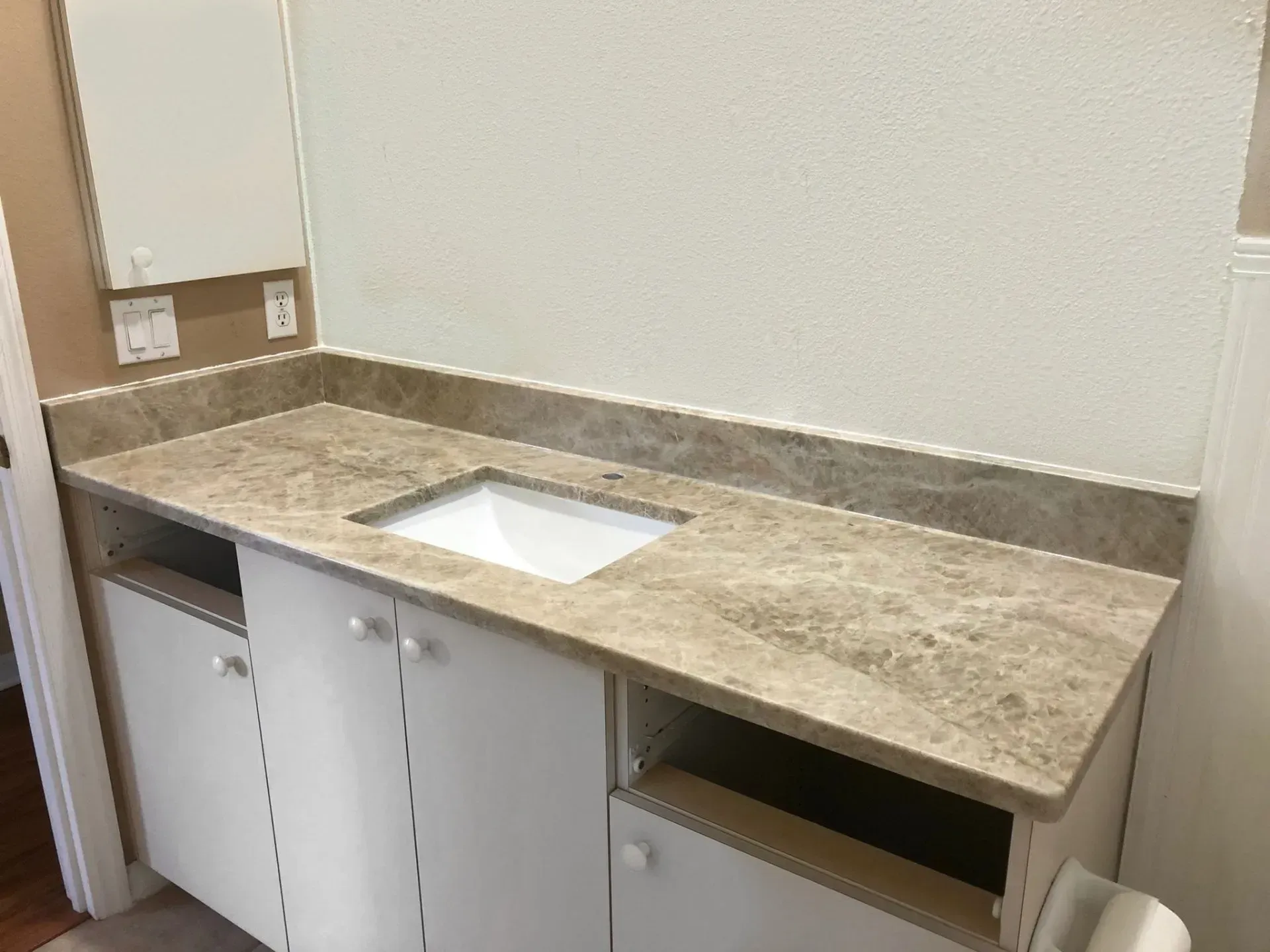 Bathroom vanity with marble countertop, white sink, and white cabinets in a corner alcove