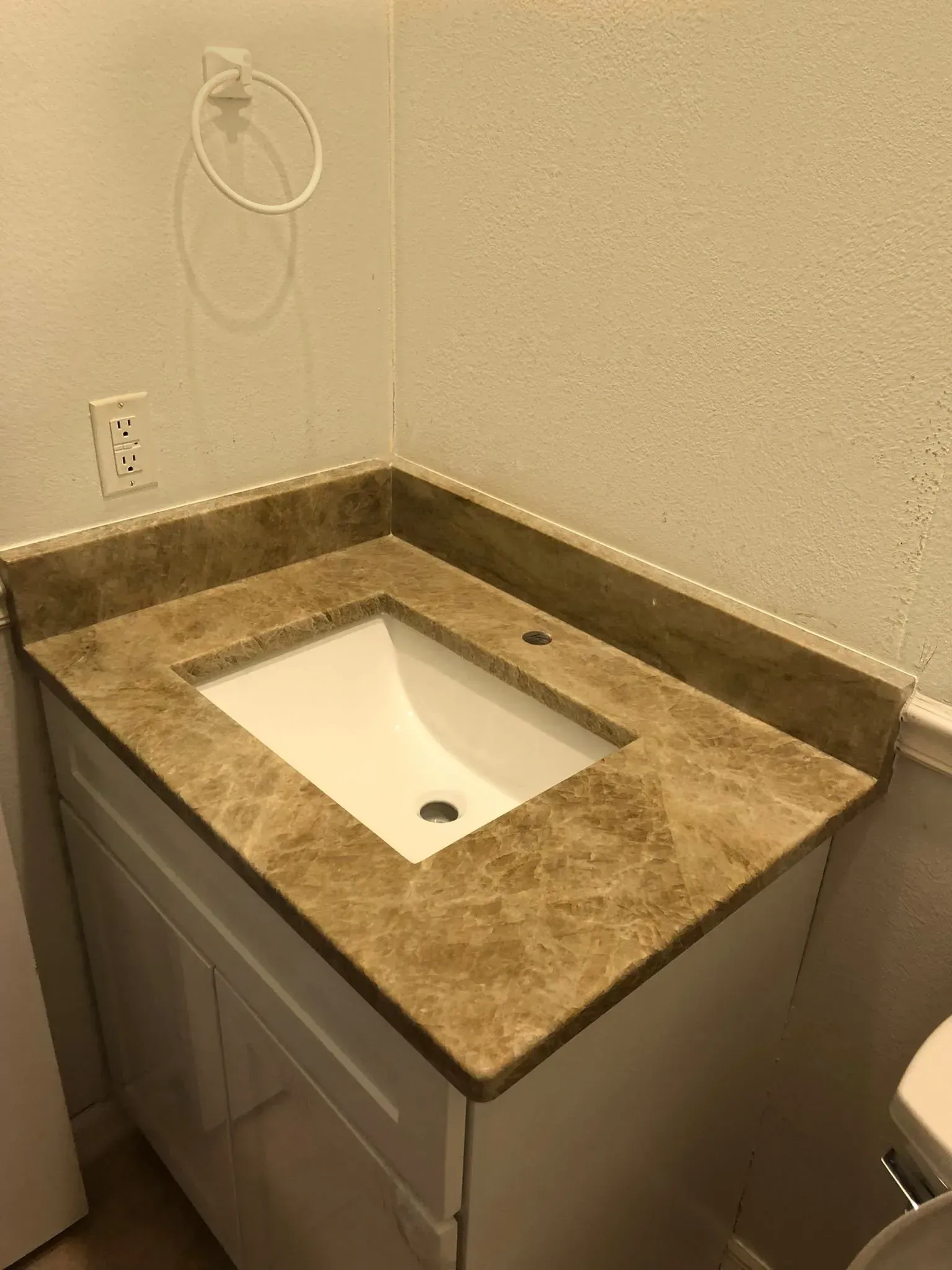Small bathroom vanity with rectangular sink, brown countertop, and wall-mounted soap dispenser.