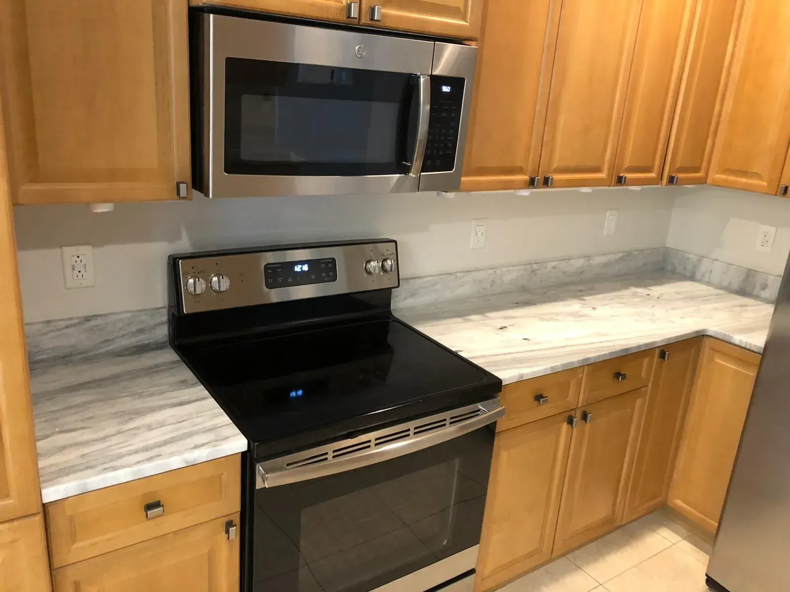 Kitchen with wood cabinets, stainless steel stove and microwave, and light marble-look countertops.