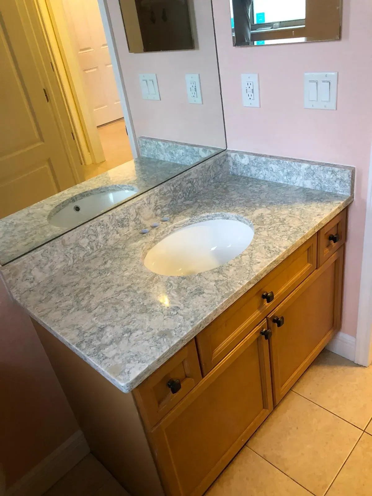 Bathroom vanity with granite countertop, oval sink, and large mirror above tiled floor.