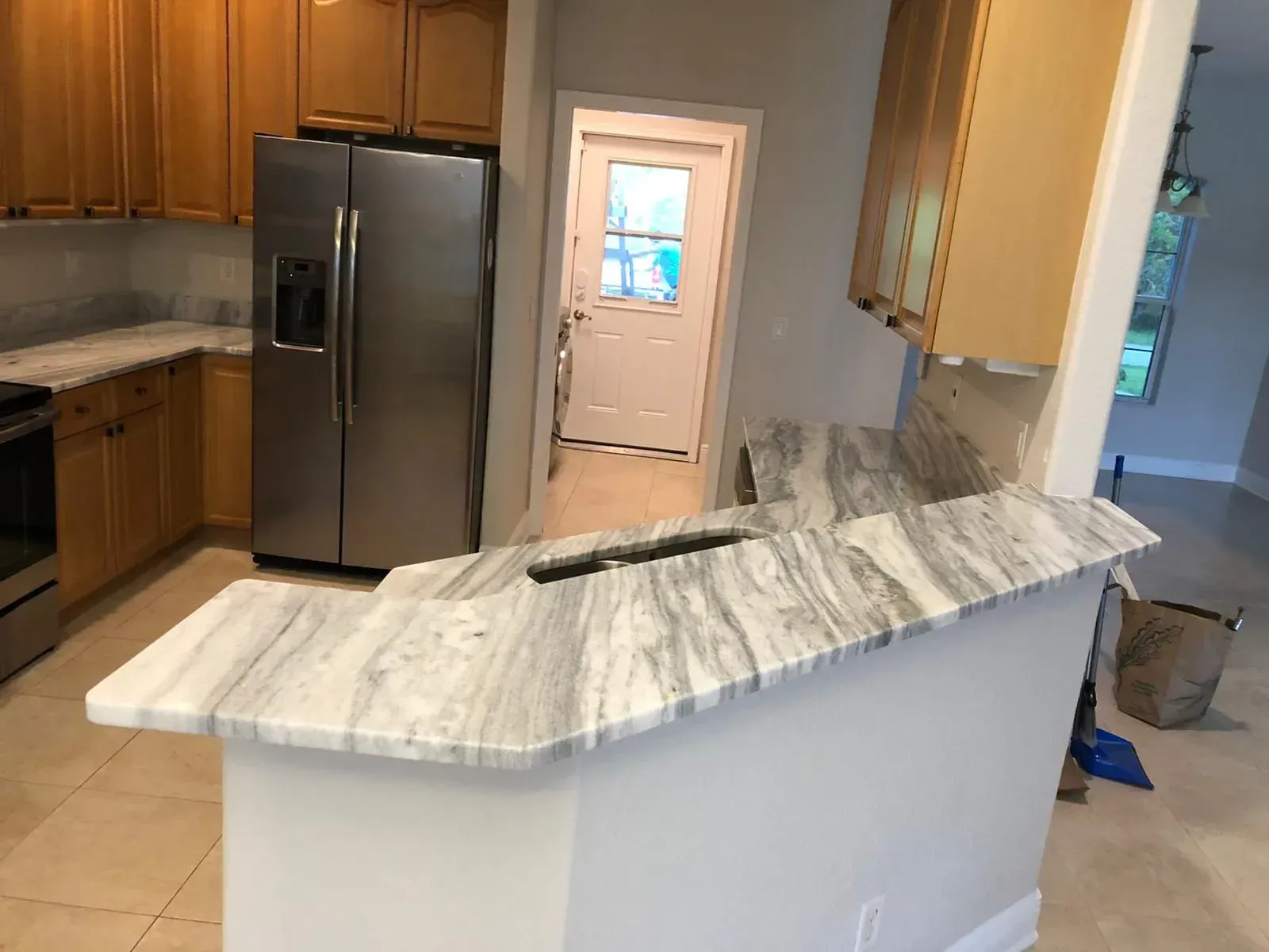 Kitchen with stainless fridge, wood cabinets, and a marble island countertop undergoing renovation.