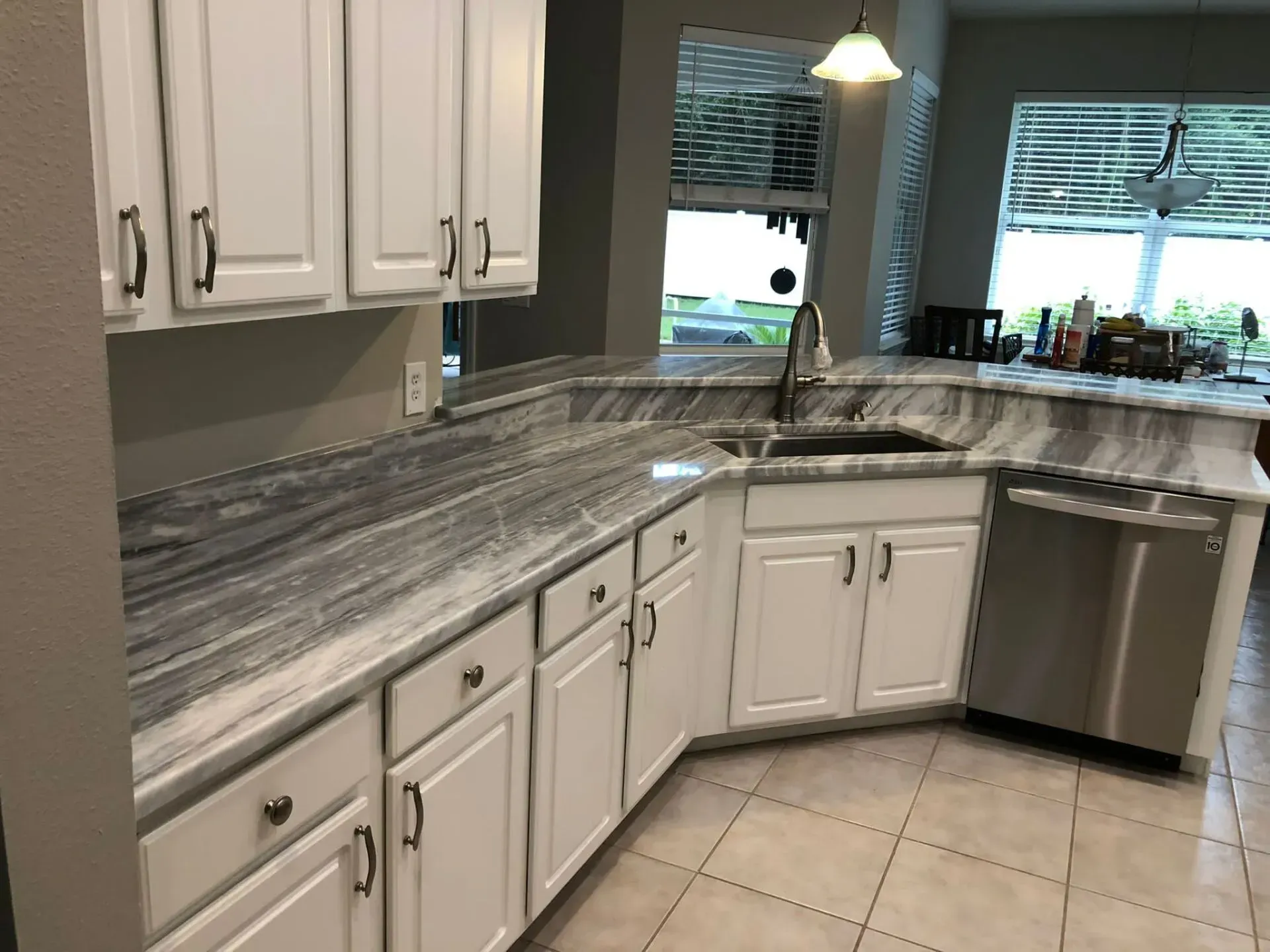 Modern kitchen with white cabinets, gray countertops, tiled floor, and stainless dishwasher by a window