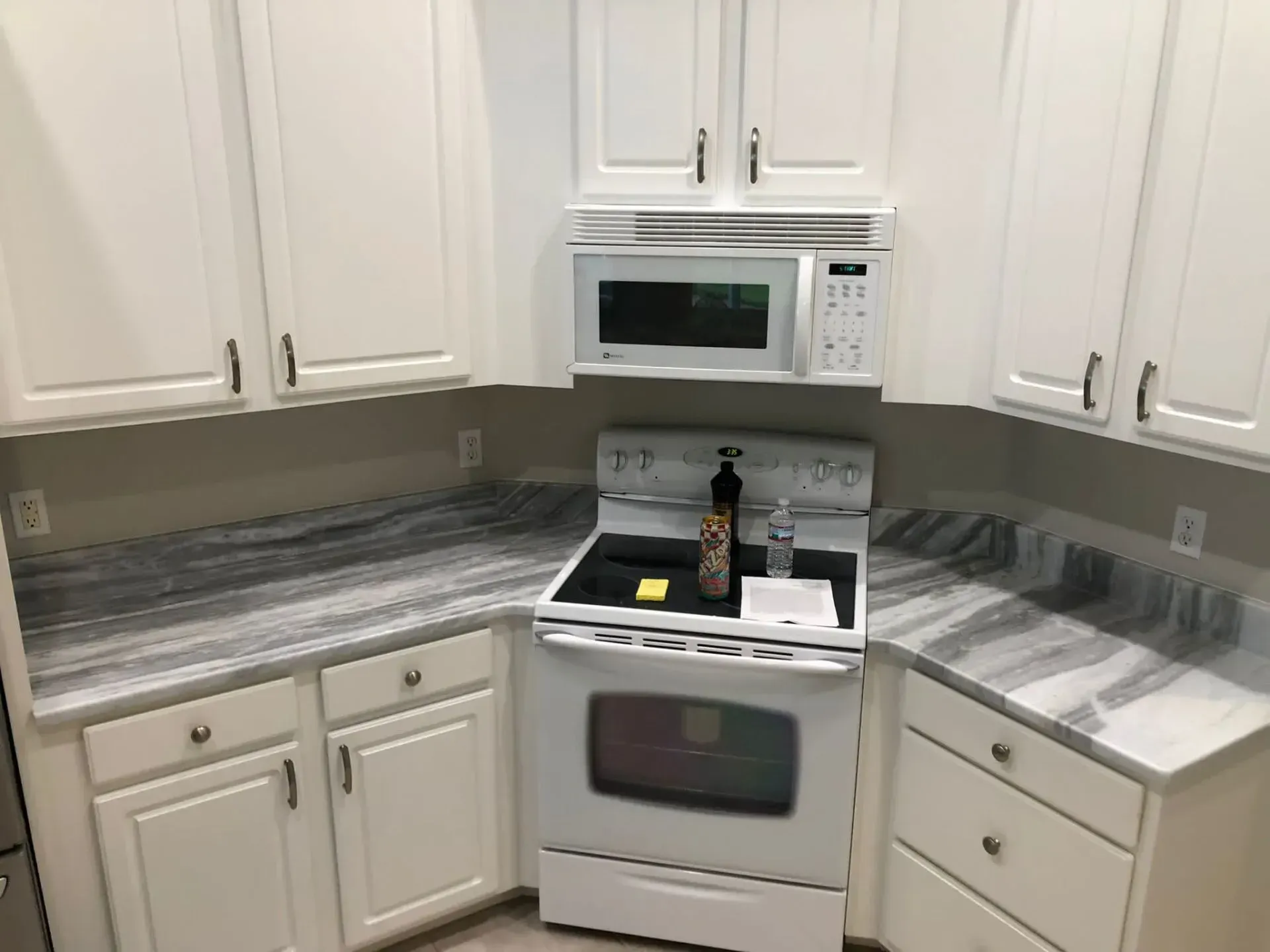 White kitchen with cabinets, gray countertops, stove, microwave, and marble-look backsplash and side counters