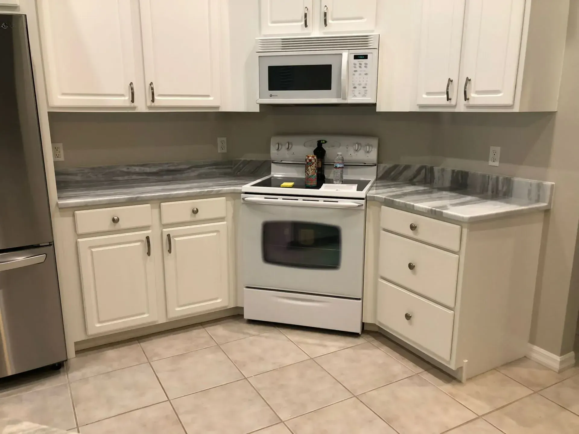 Small white kitchen with cabinets, stove, microwave, and tiled floor.