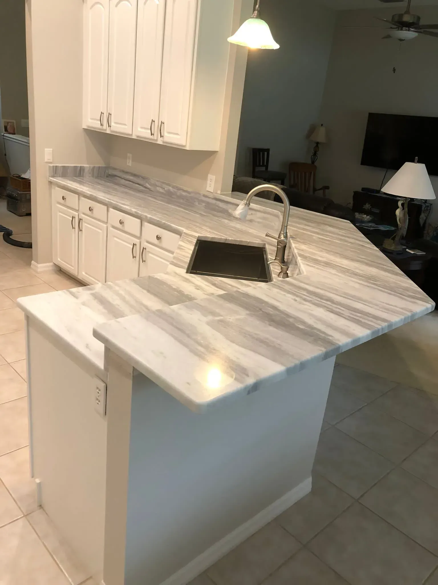 Kitchen island with marble countertop, sink, and white cabinets in a home interior