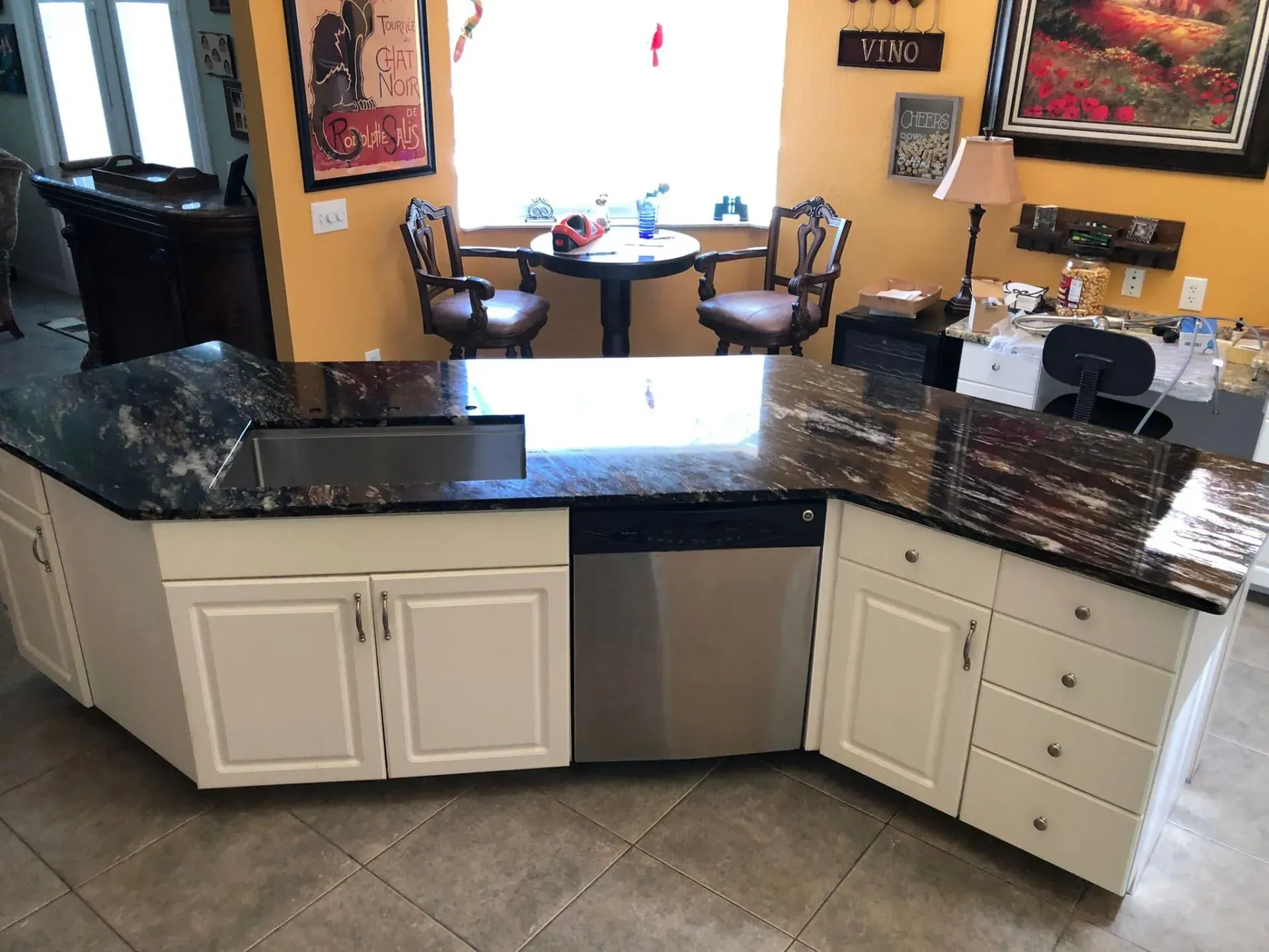 Kitchen with a curved granite island, white cabinets, stainless dishwasher, and tiled floor.