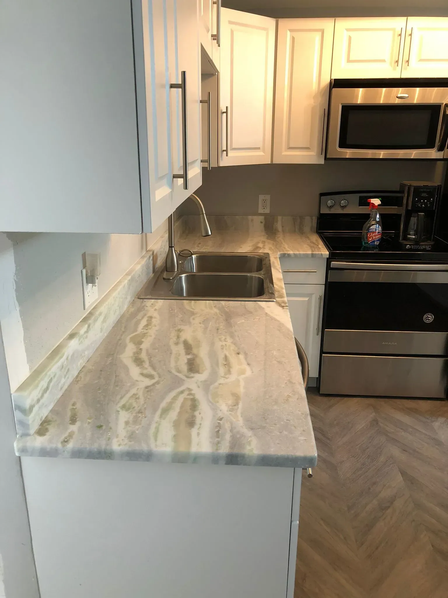 Modern kitchen with marble countertop, white cabinets, sink, and stainless steel appliances.