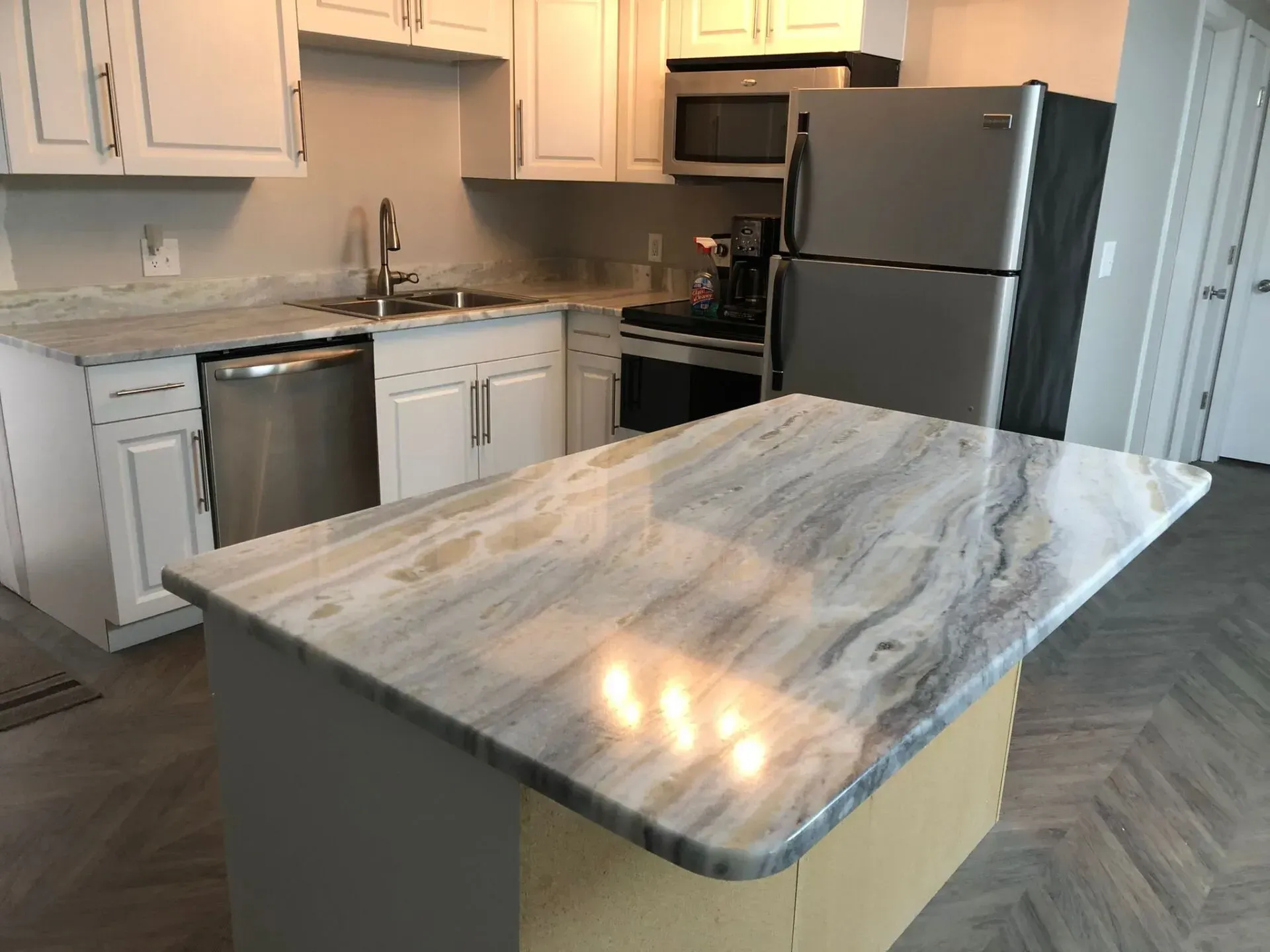Kitchen with marble-topped island, white cabinets, stainless dishwasher, and black refrigerator.