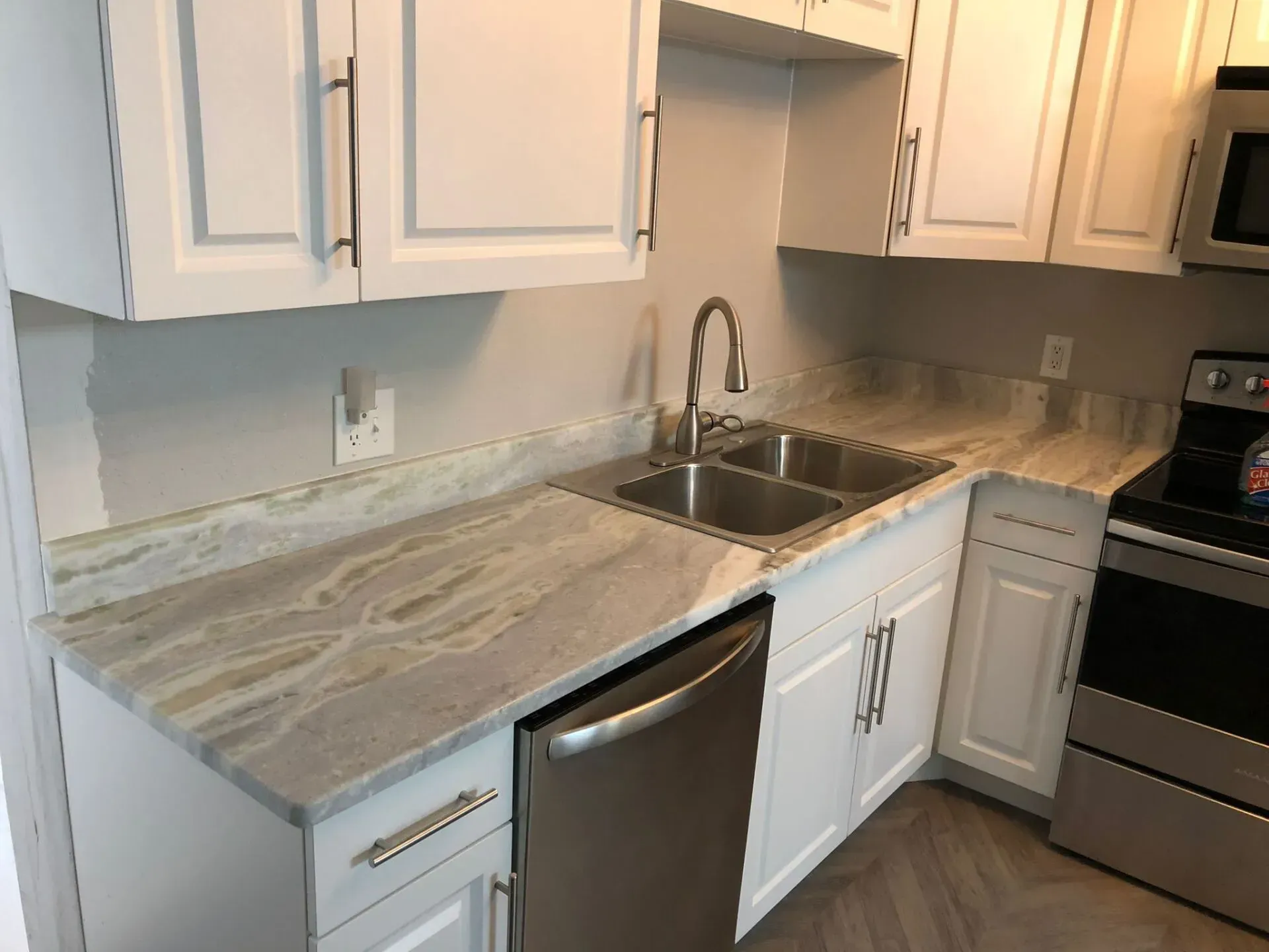 Small kitchen with white cabinets, gray countertop, sink, dishwasher, and stainless-steel stove.