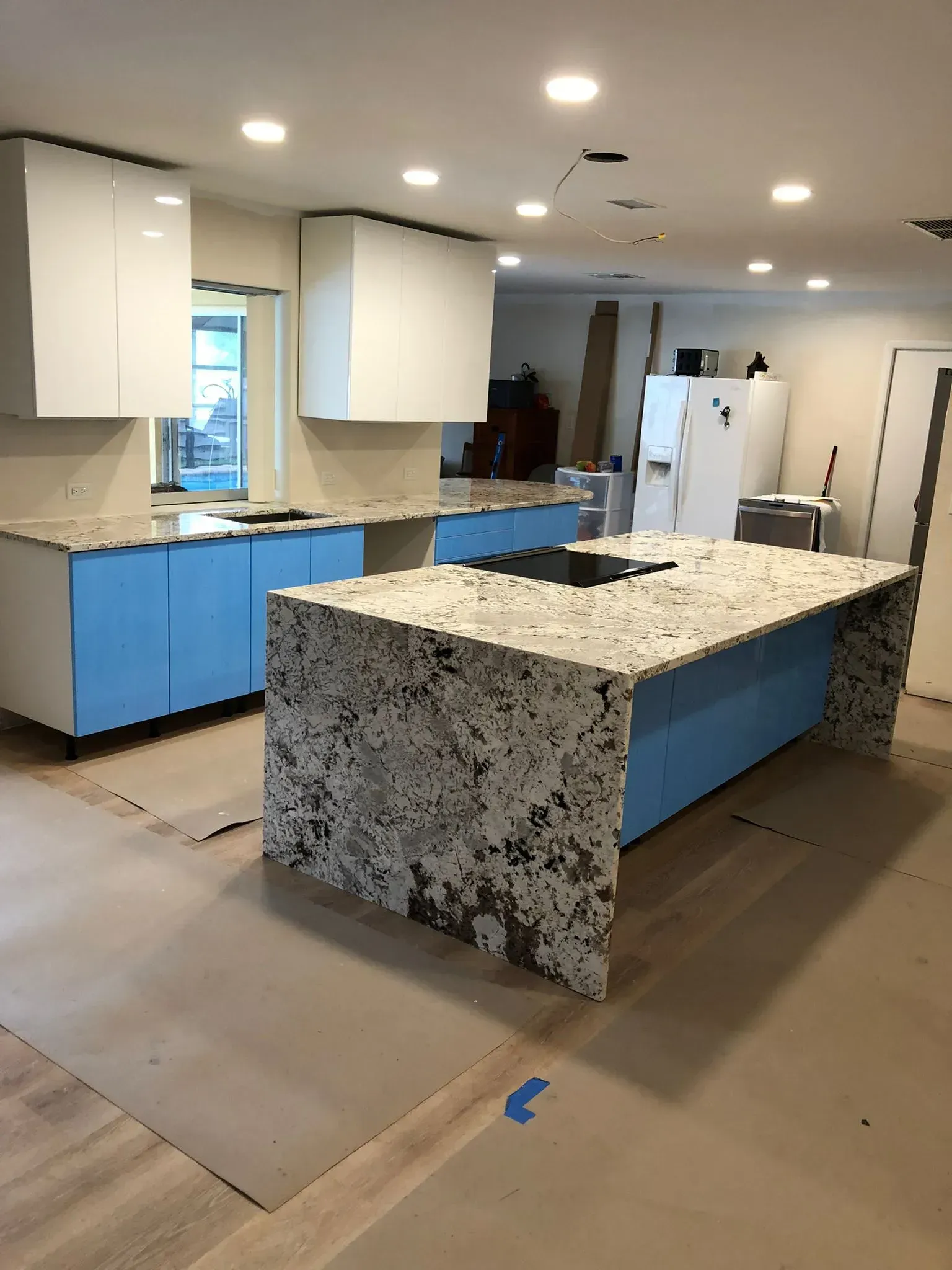 Modern kitchen with white cabinets, blue lower drawers, and a granite island under recessed ceiling lights