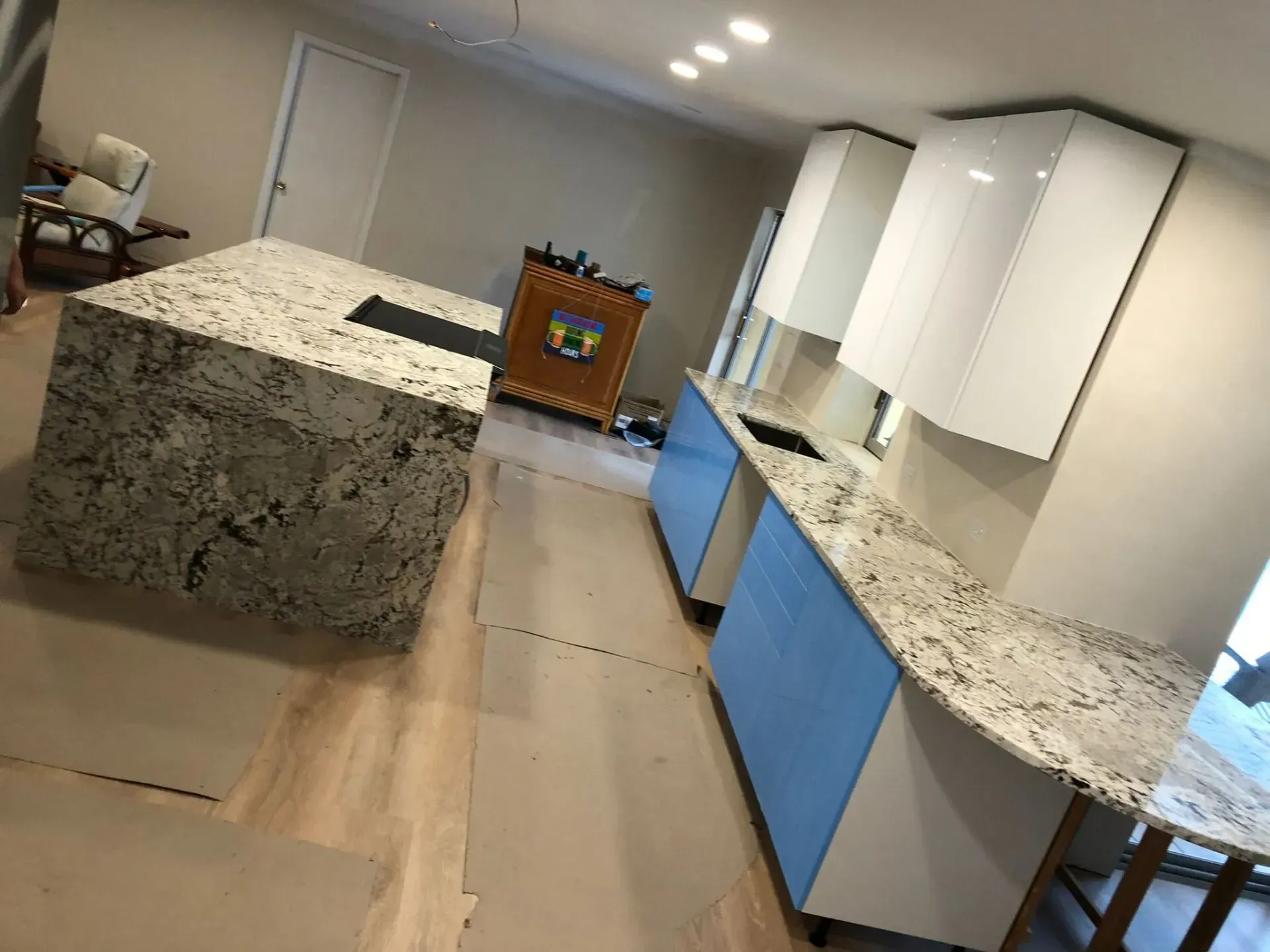 Modern kitchen with granite island and countertops, white cabinets, and blue lower cabinets in bright room