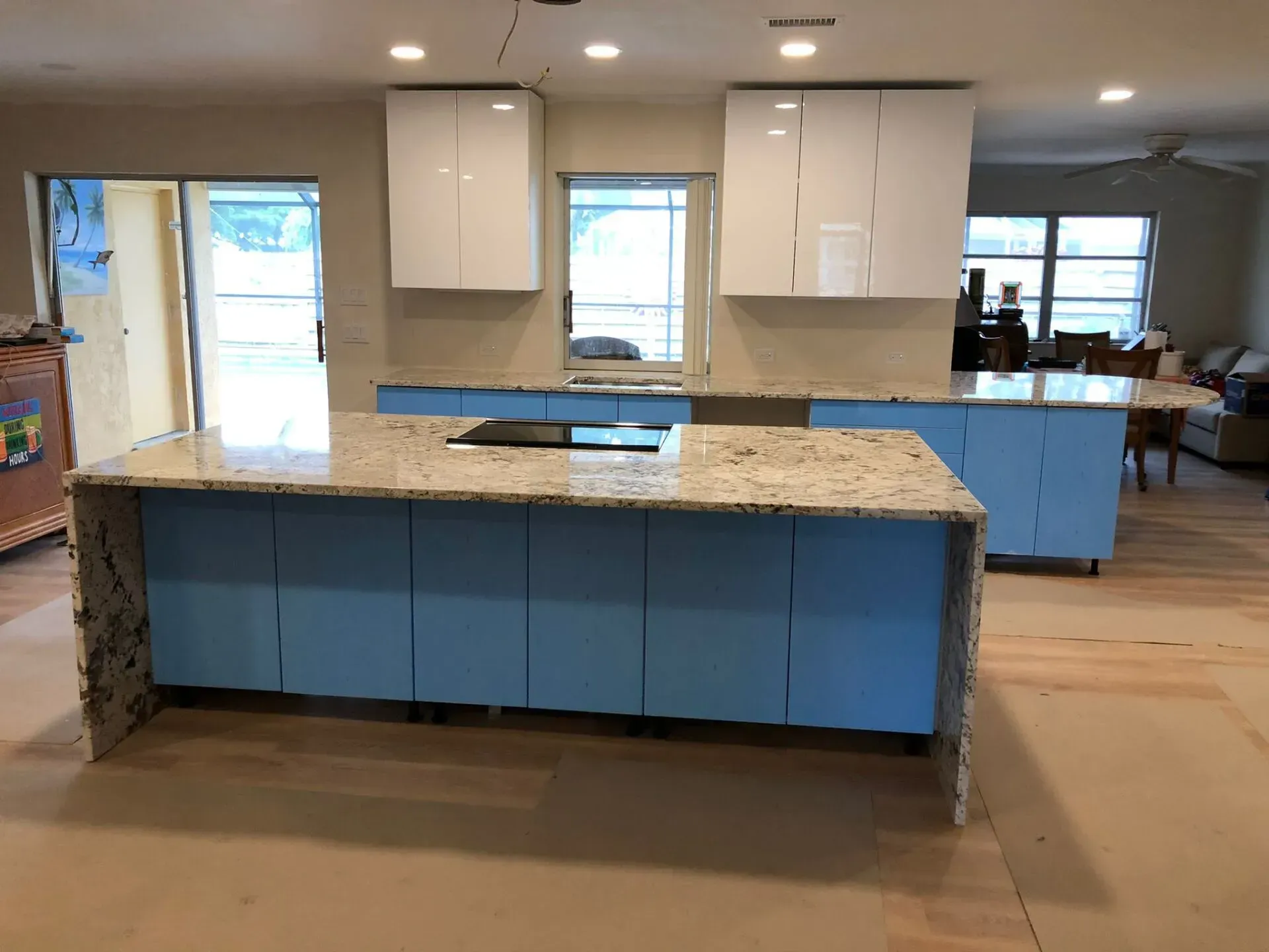 Modern kitchen with blue cabinets, granite island, and white upper cabinets in a bright room.