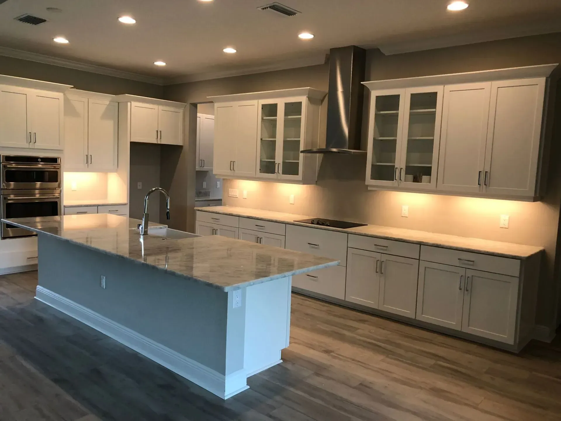 Modern kitchen with white cabinets, large island, granite counters, and warm under-cabinet lighting.