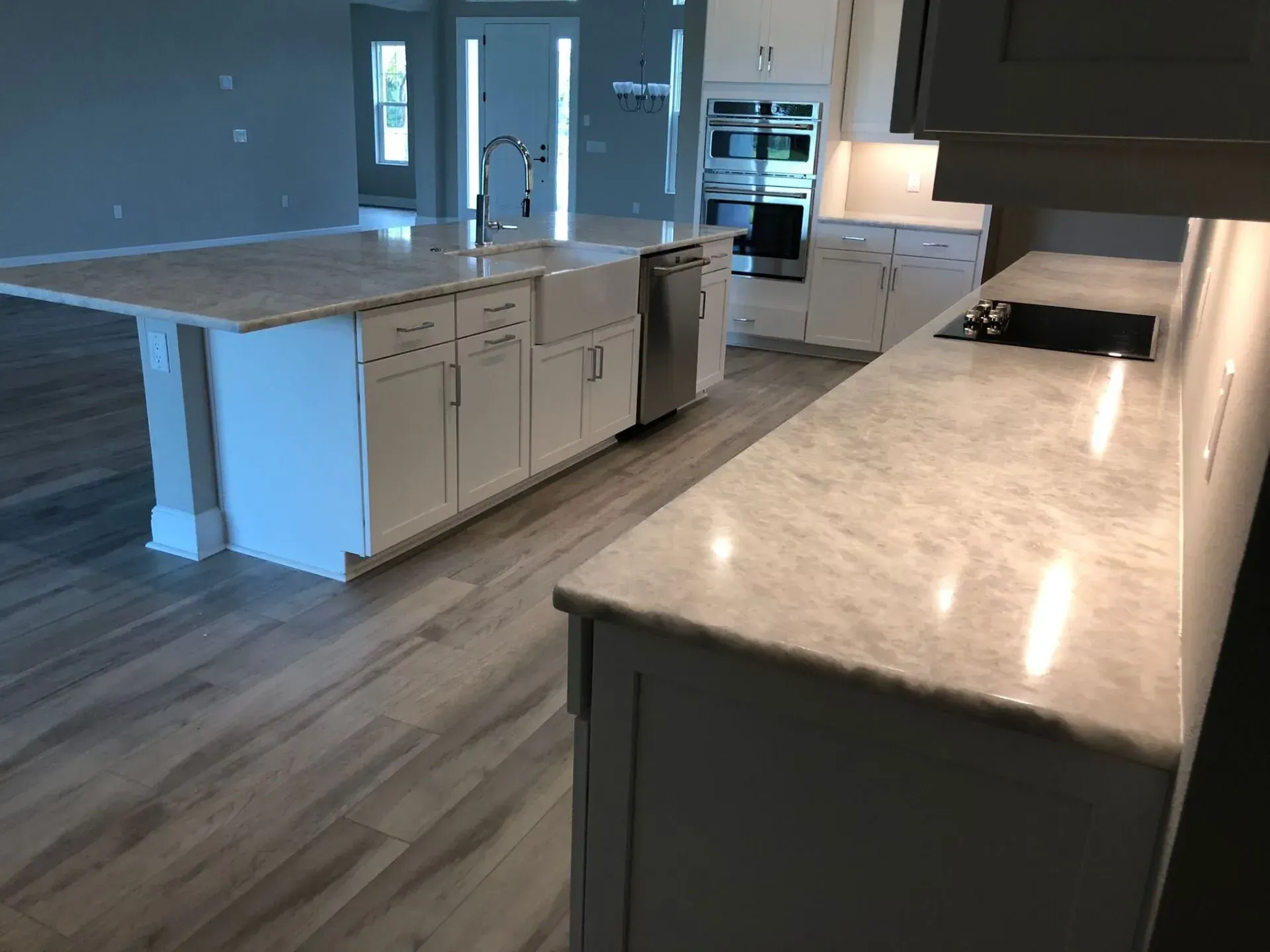Modern kitchen with marble island, wood floors, and stainless appliances, viewed from the counter.
