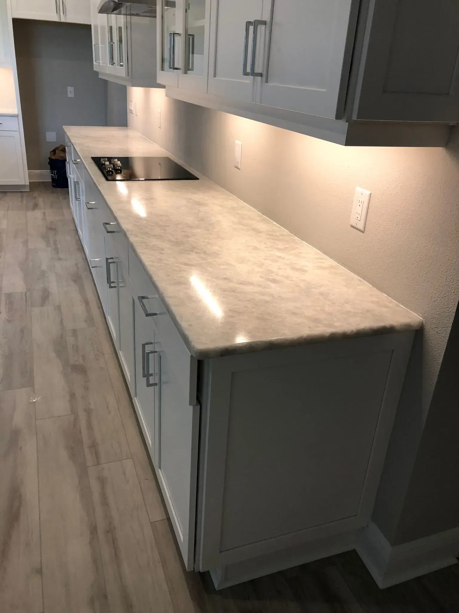Modern kitchen with gray cabinets, light countertop, and built-in stovetop along a hallway.