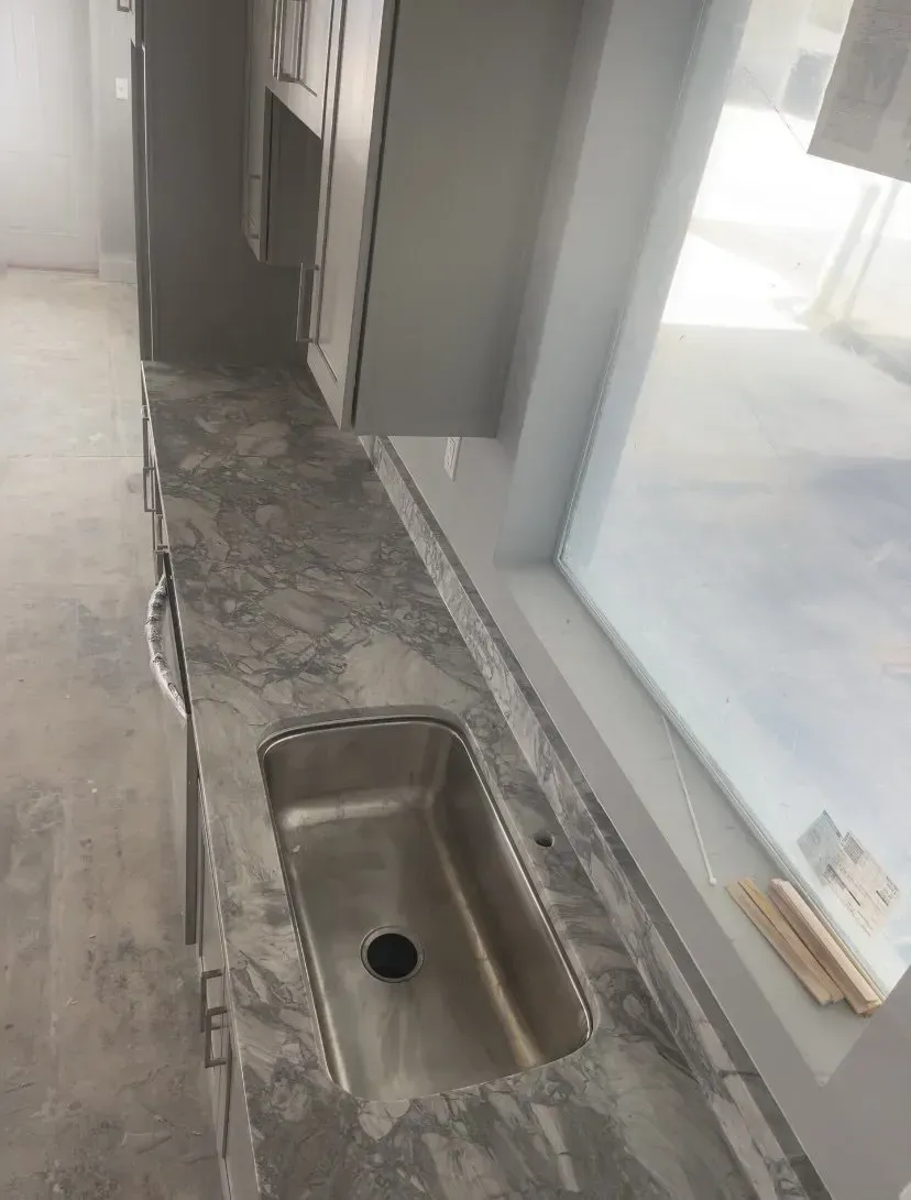 Countertop with a built-in sink under a window in an unfinished room.