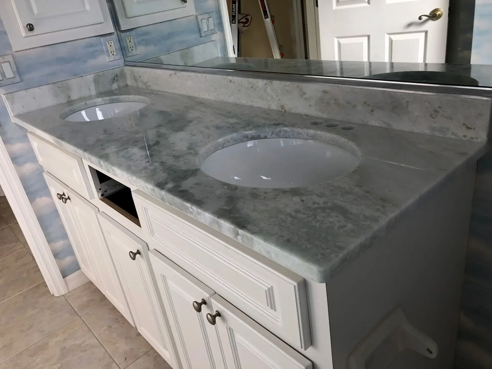 Marble bathroom vanity with double sinks, white cabinets, and a large mirror.
