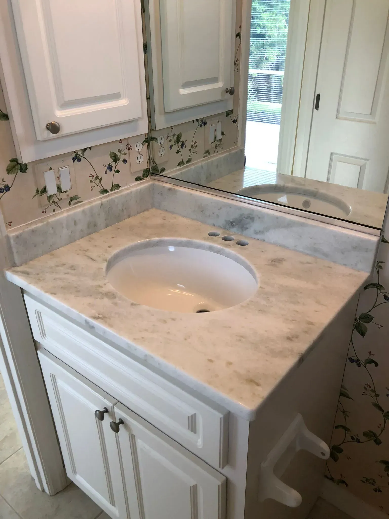 Bathroom vanity with marble countertop and oval sink, white cabinets, and mirror above.