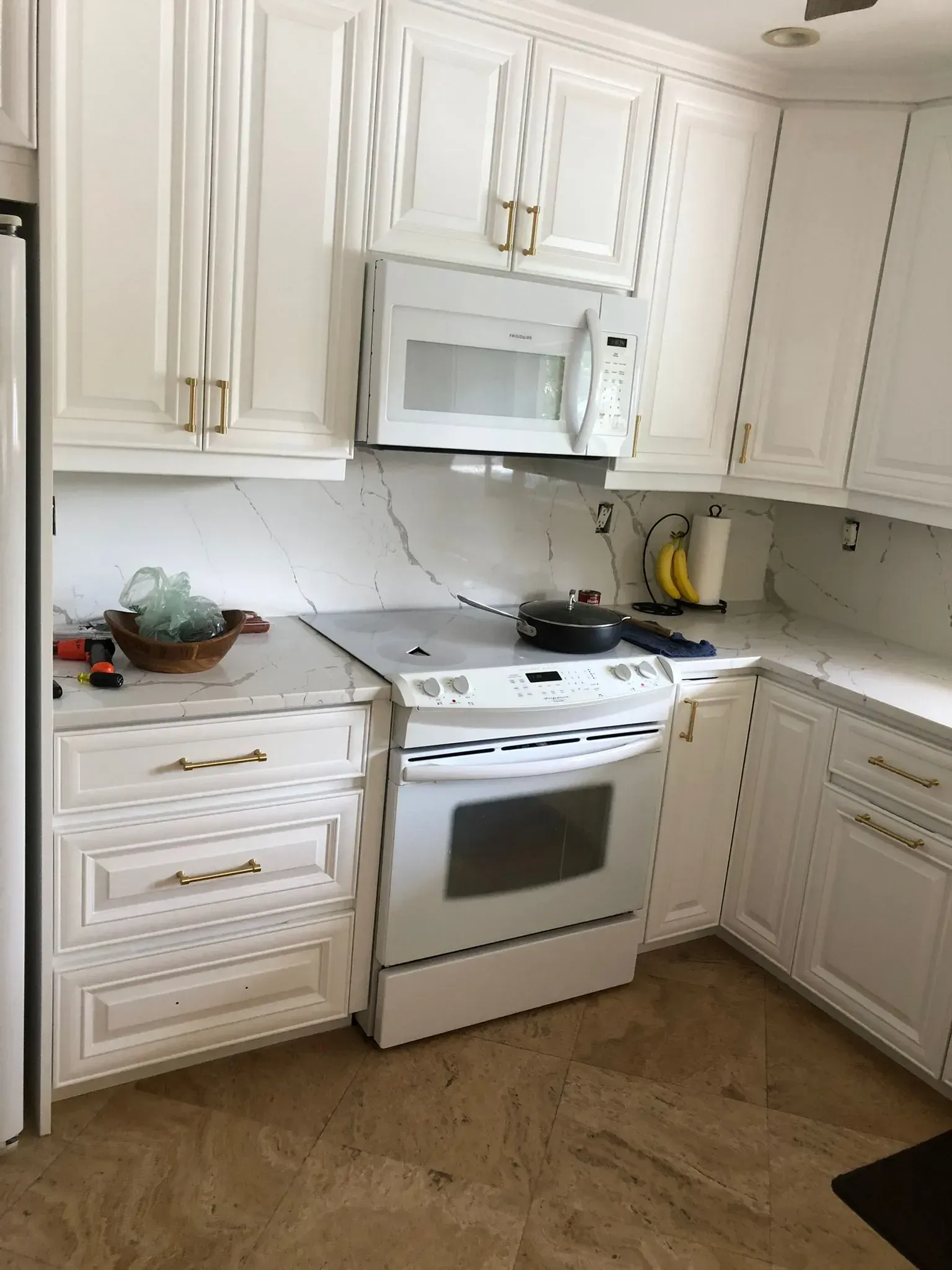 White kitchen with stove, microwave, corner cabinets, marble backsplash, and wood-look floor