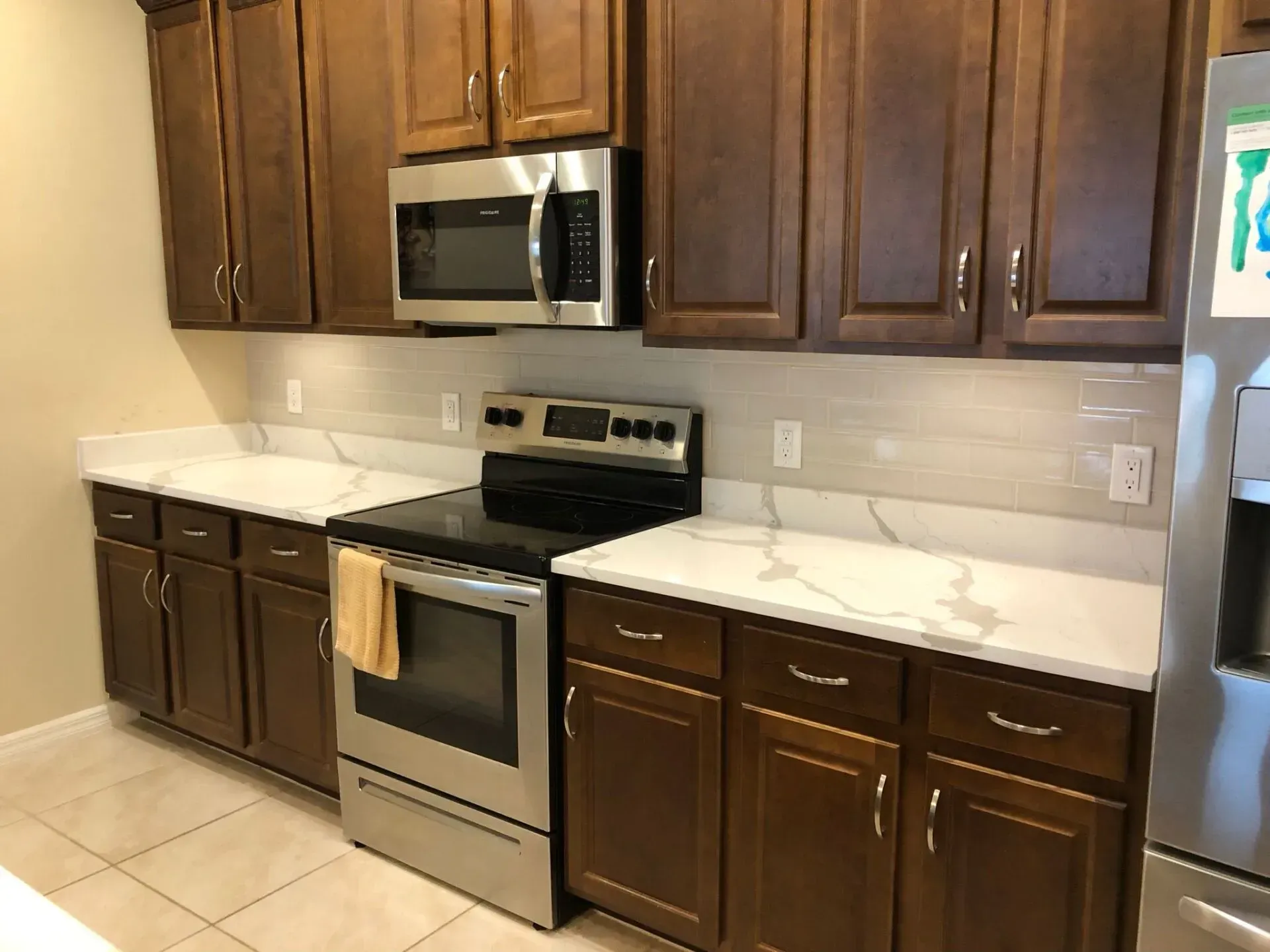 Modern kitchen with dark wood cabinets, stainless steel oven and microwave, and white countertops.