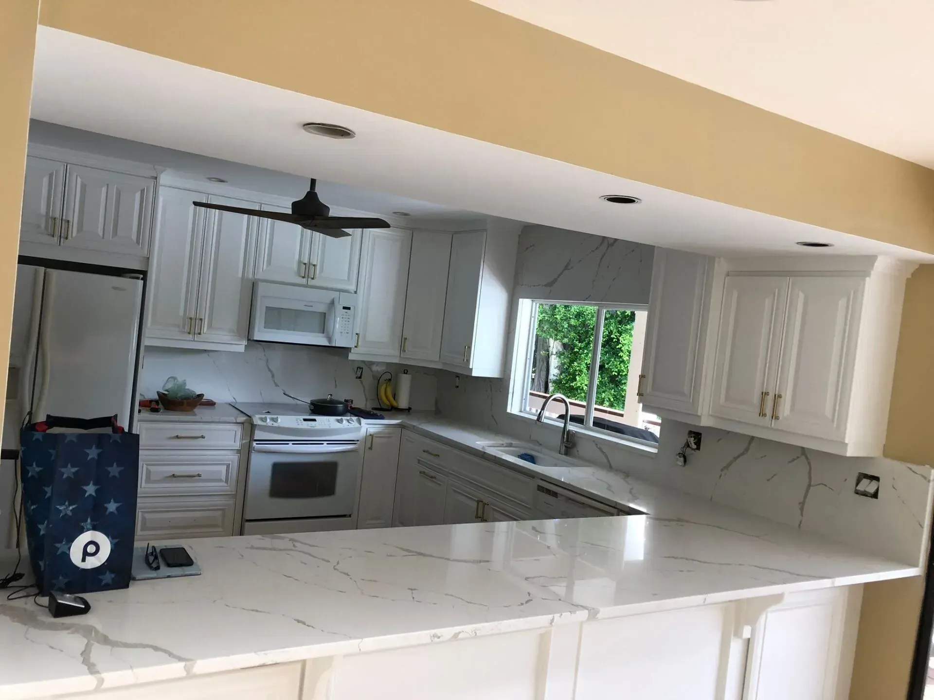 Bright kitchen with white cabinets, marble counters, and a window over the sink