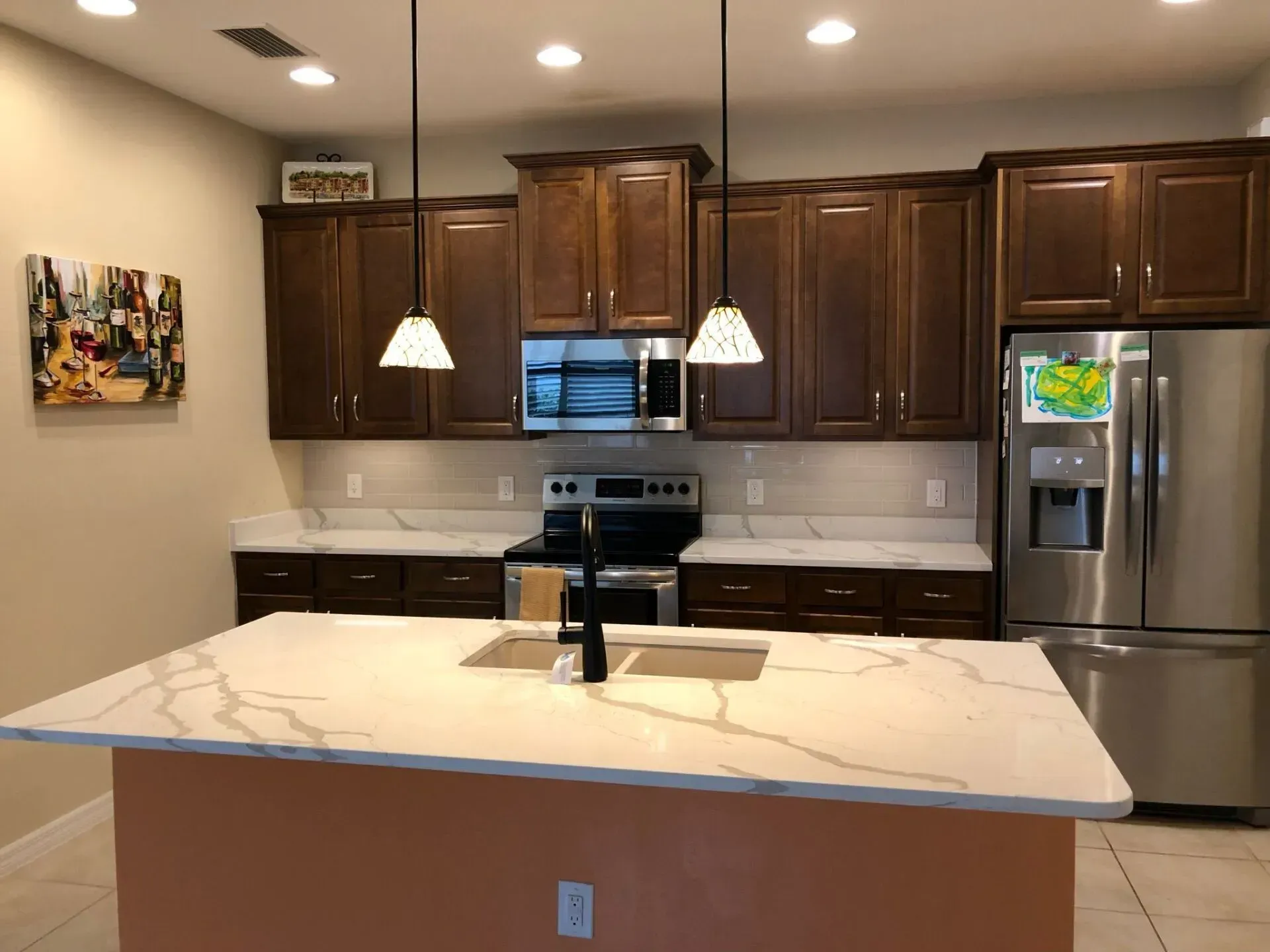Modern kitchen with dark wood cabinets, marble island, pendant lights, and stainless steel refrigerator