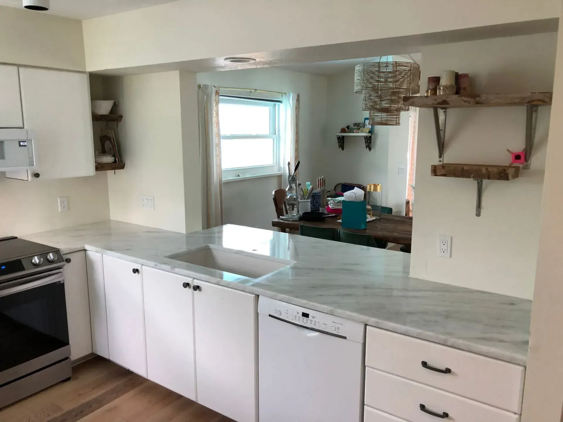 Bright kitchen with white cabinets, gray countertops, stove, sink, and open wall shelves