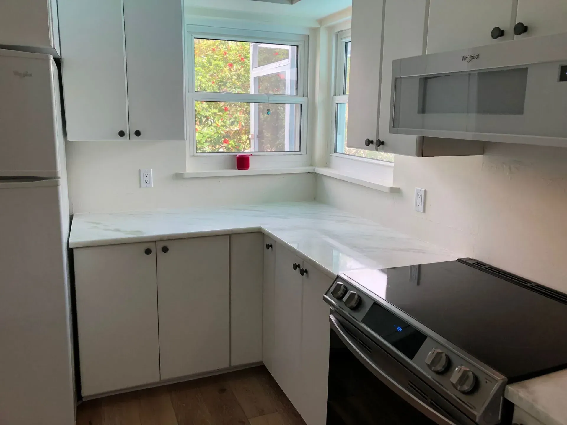 Bright white kitchen with L-shaped counters, stainless stove, gray cabinets, and a window over the sink.