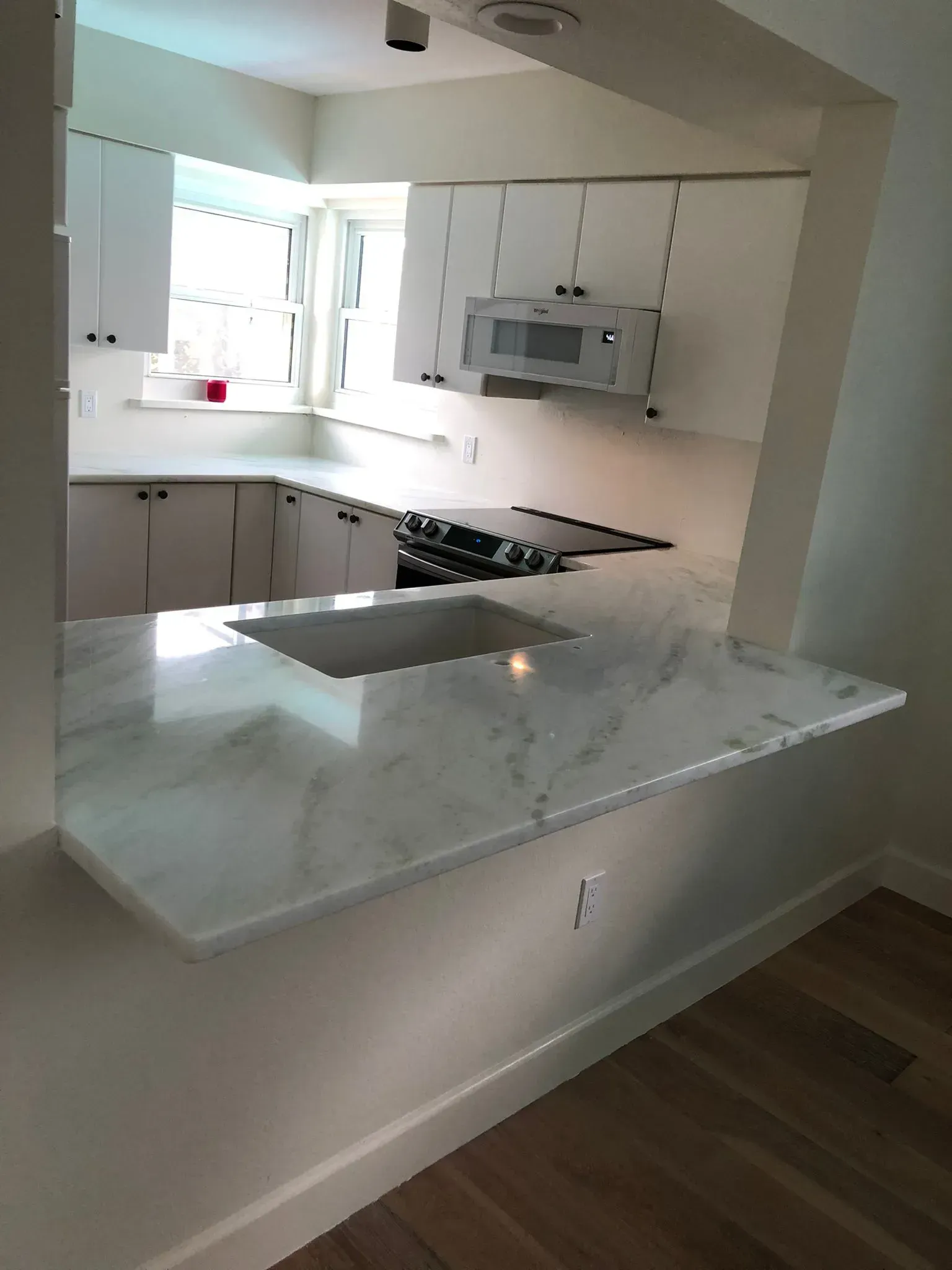 Modern kitchen with white cabinets, marble counter, and black gas stove, viewed from a breakfast bar.