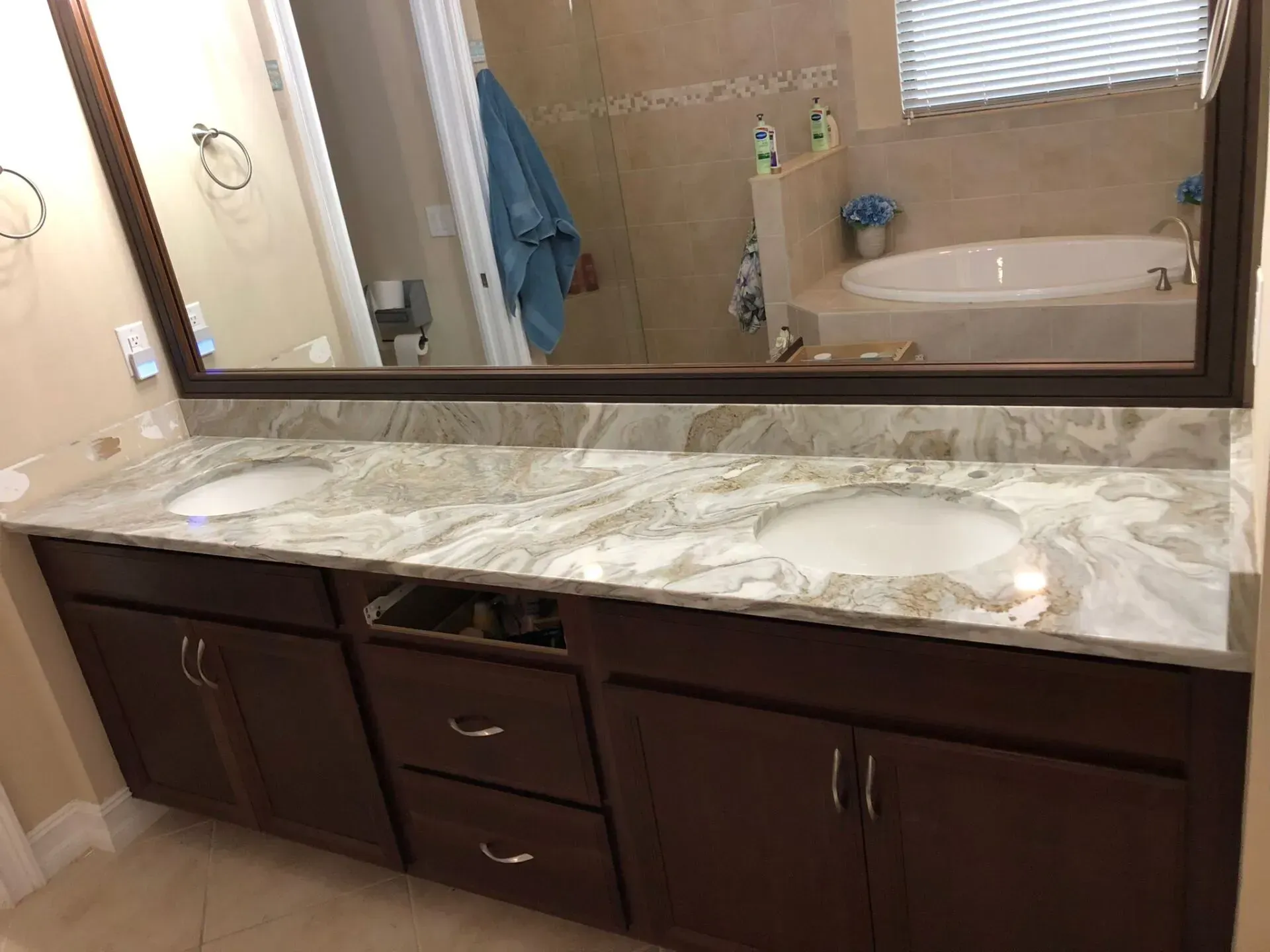 Bathroom vanity with marble countertop, large mirror, double sinks, and dark wood cabinets