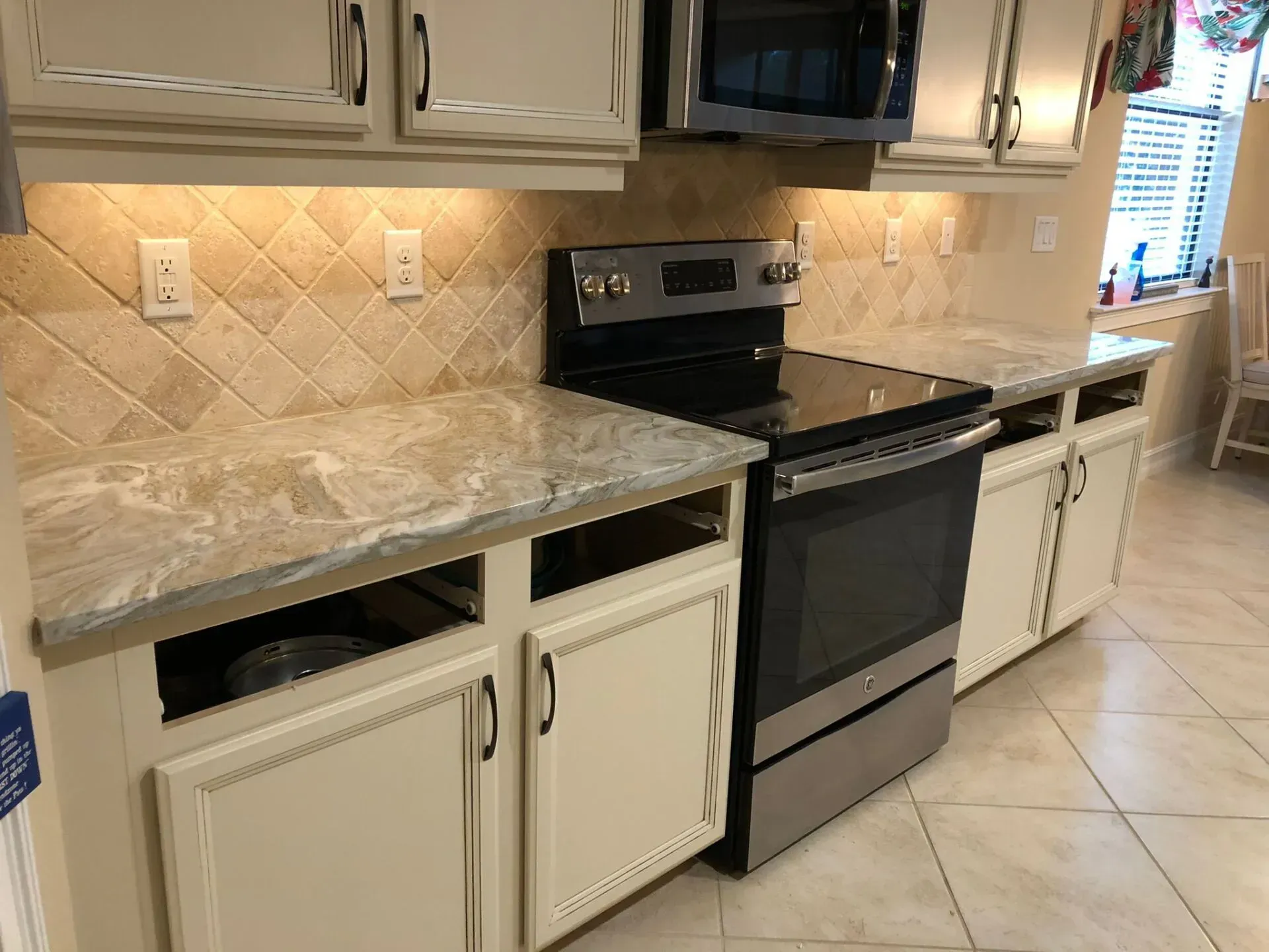 Kitchen with beige tile countertops, white cabinets, and a black stove with a microwave above it.