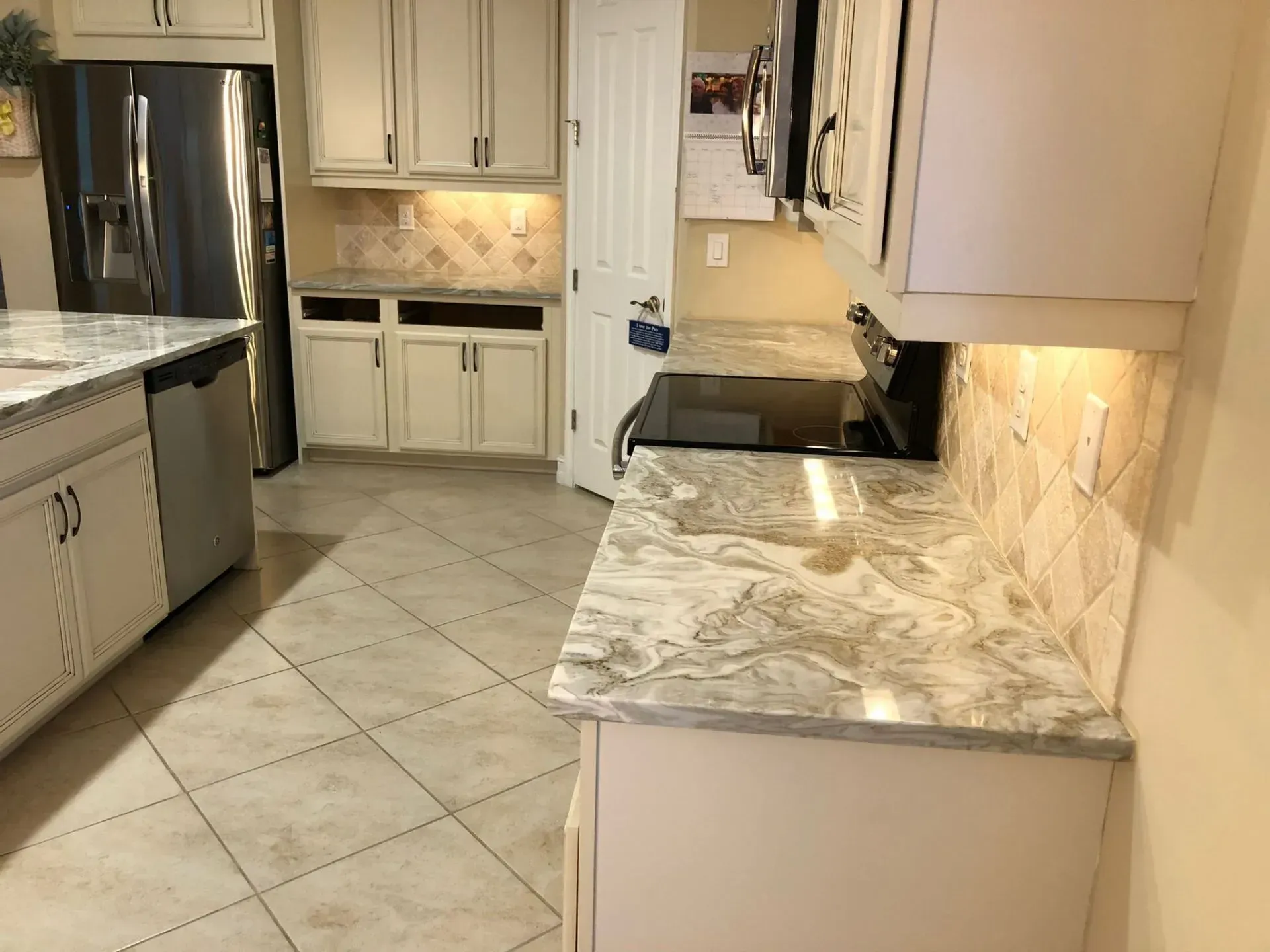 Bright kitchen with white cabinets, marble countertops, stainless fridge, and tiled floor