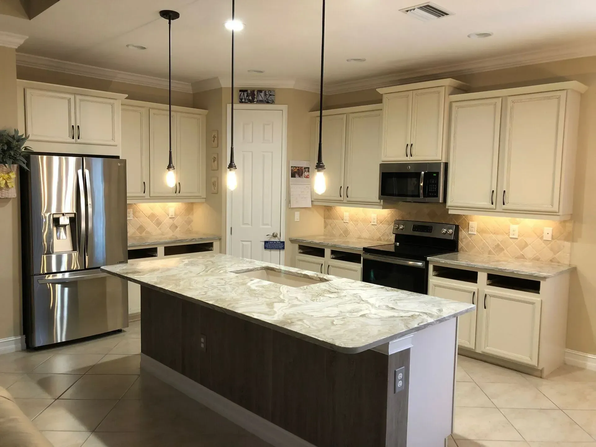 Spacious cream-colored kitchen with stainless steel appliances, island, and tiled floor.