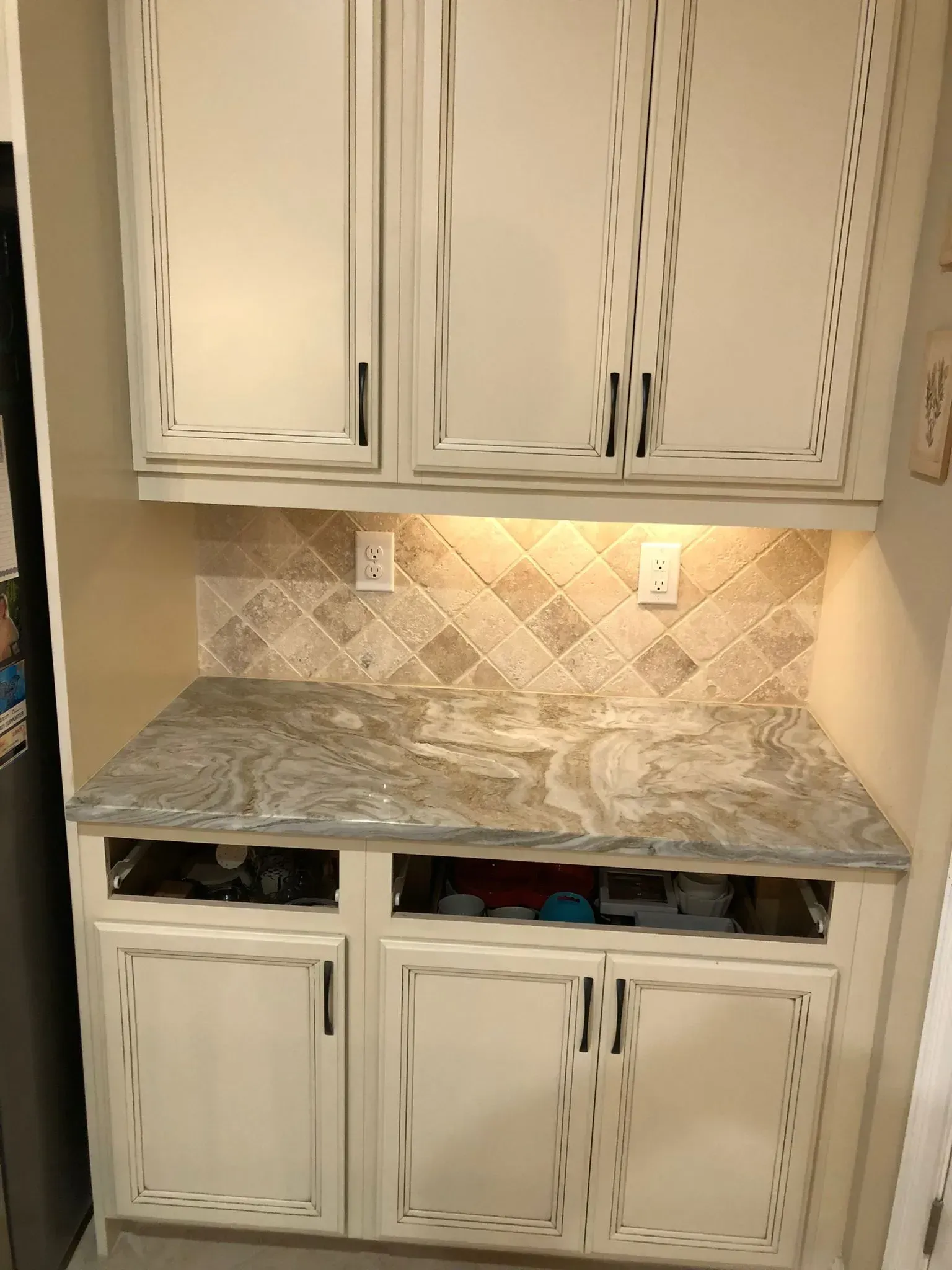 Built-in kitchen cabinets with marble-look countertop and tile backsplash under under-cabinet lights