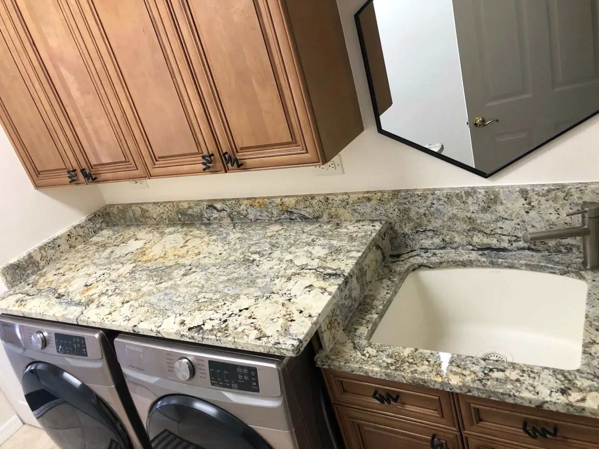 Kitchen with granite countertop, double sink, wood cabinets, and washer and dryer beneath the counter.