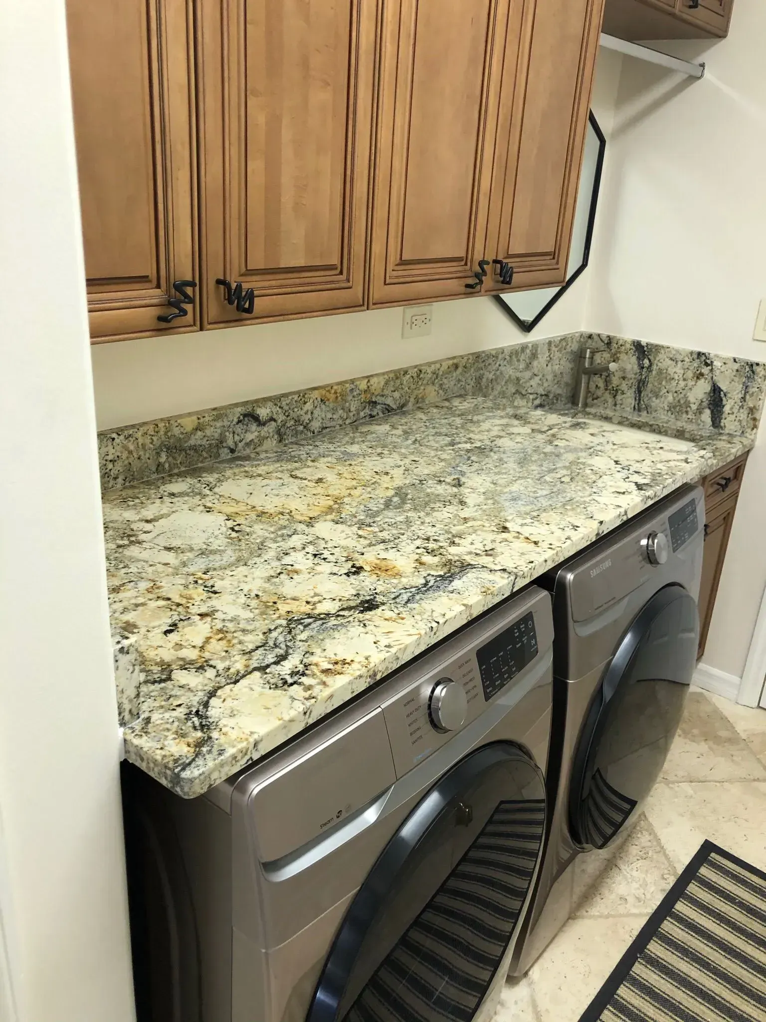 Laundry room countertop with speckled granite over washer and dryer, under wooden cabinets