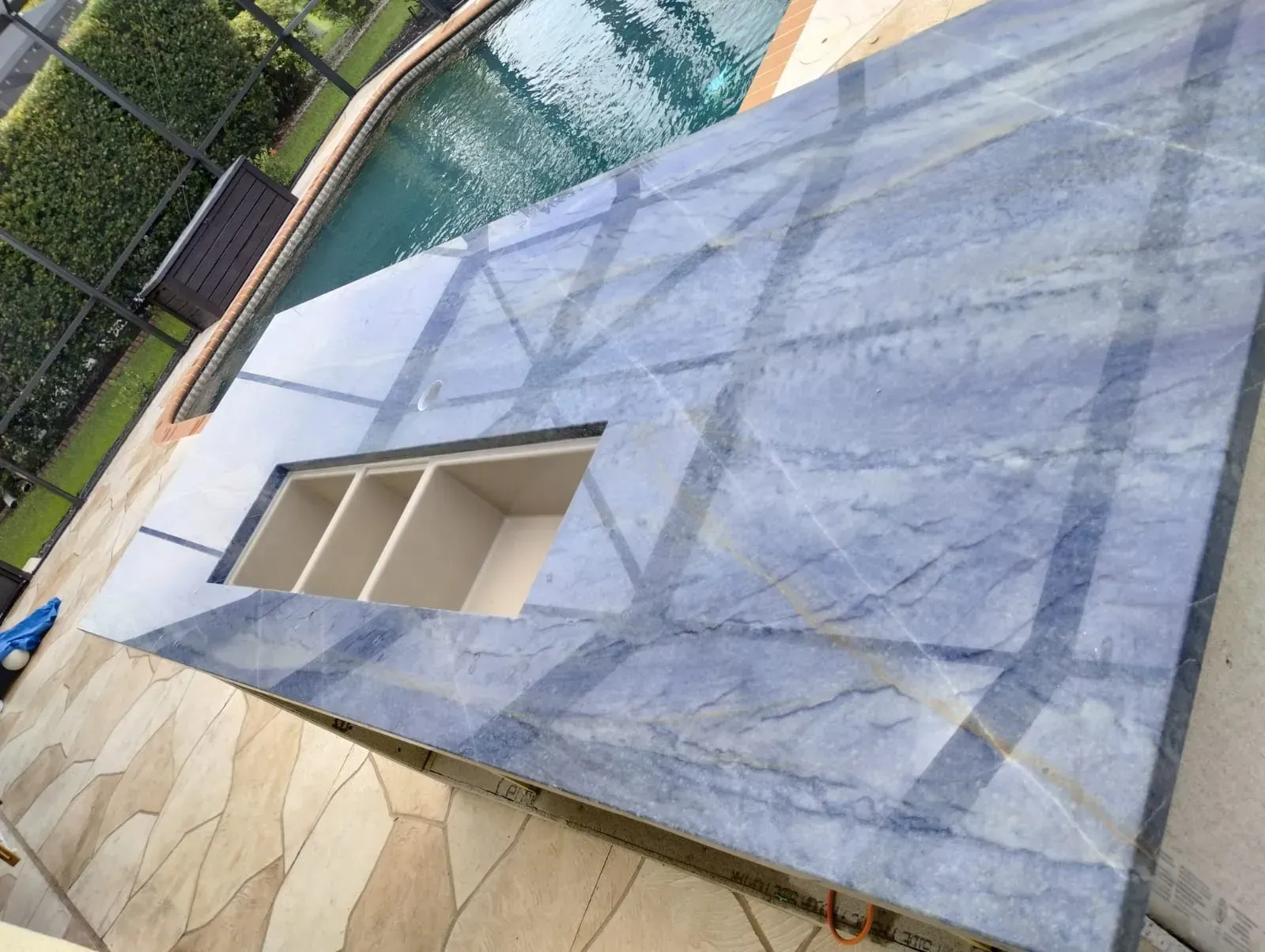 Blue poolside patio with a built-in rectangular fire pit beside a turquoise swimming pool.