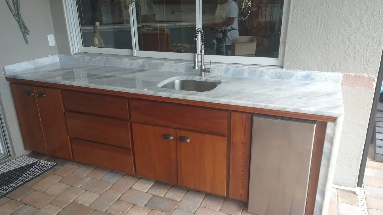Outdoor wooden kitchen cabinet with marble countertop and sink under a window