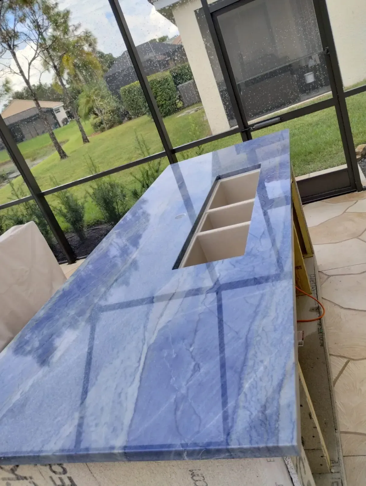 Blue covered tabletop with rectangular cutouts on a screened patio, near a backyard lawn.