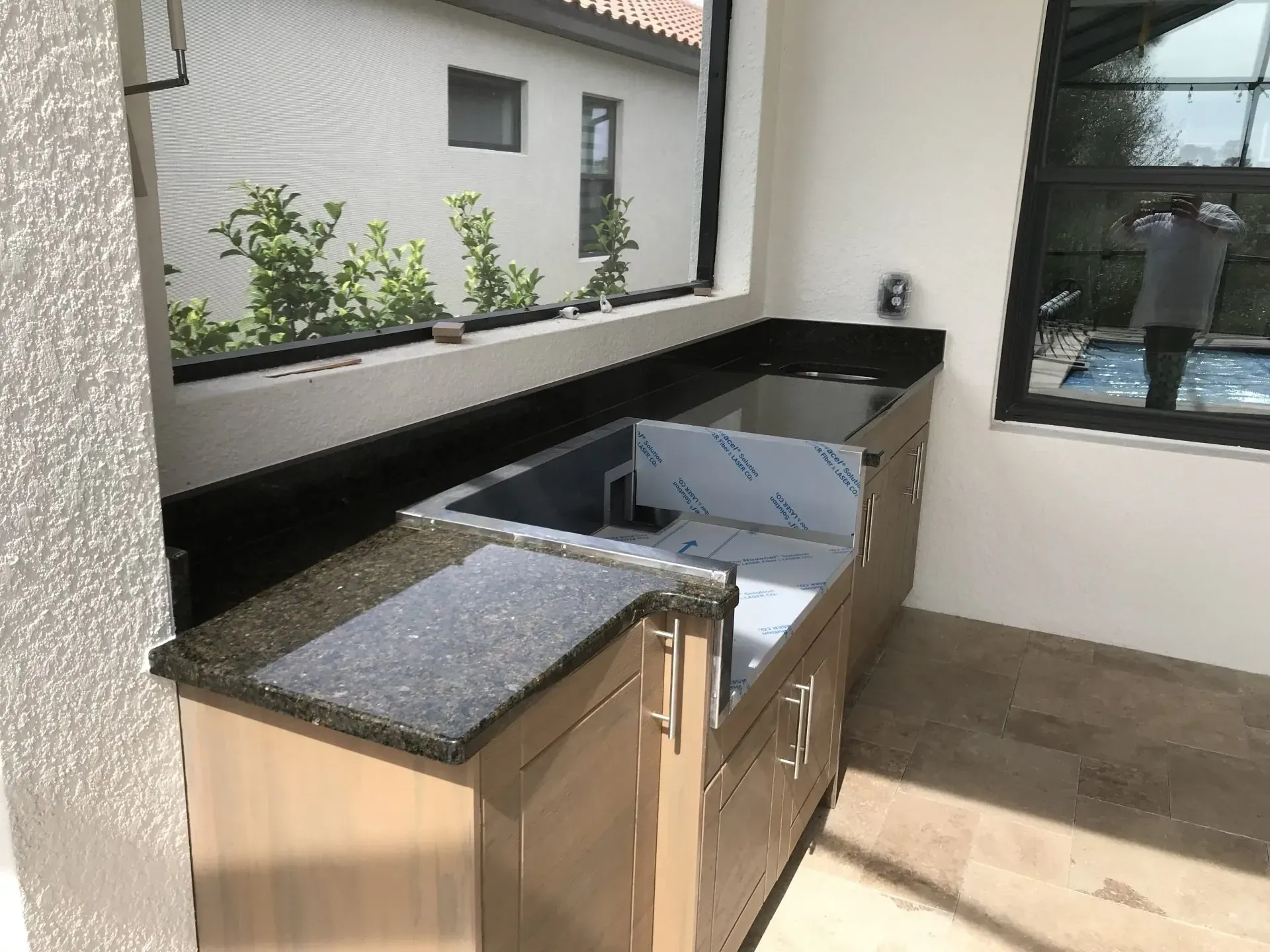 Modern outdoor kitchen with granite counter, sink, and built-in grill under a covered patio