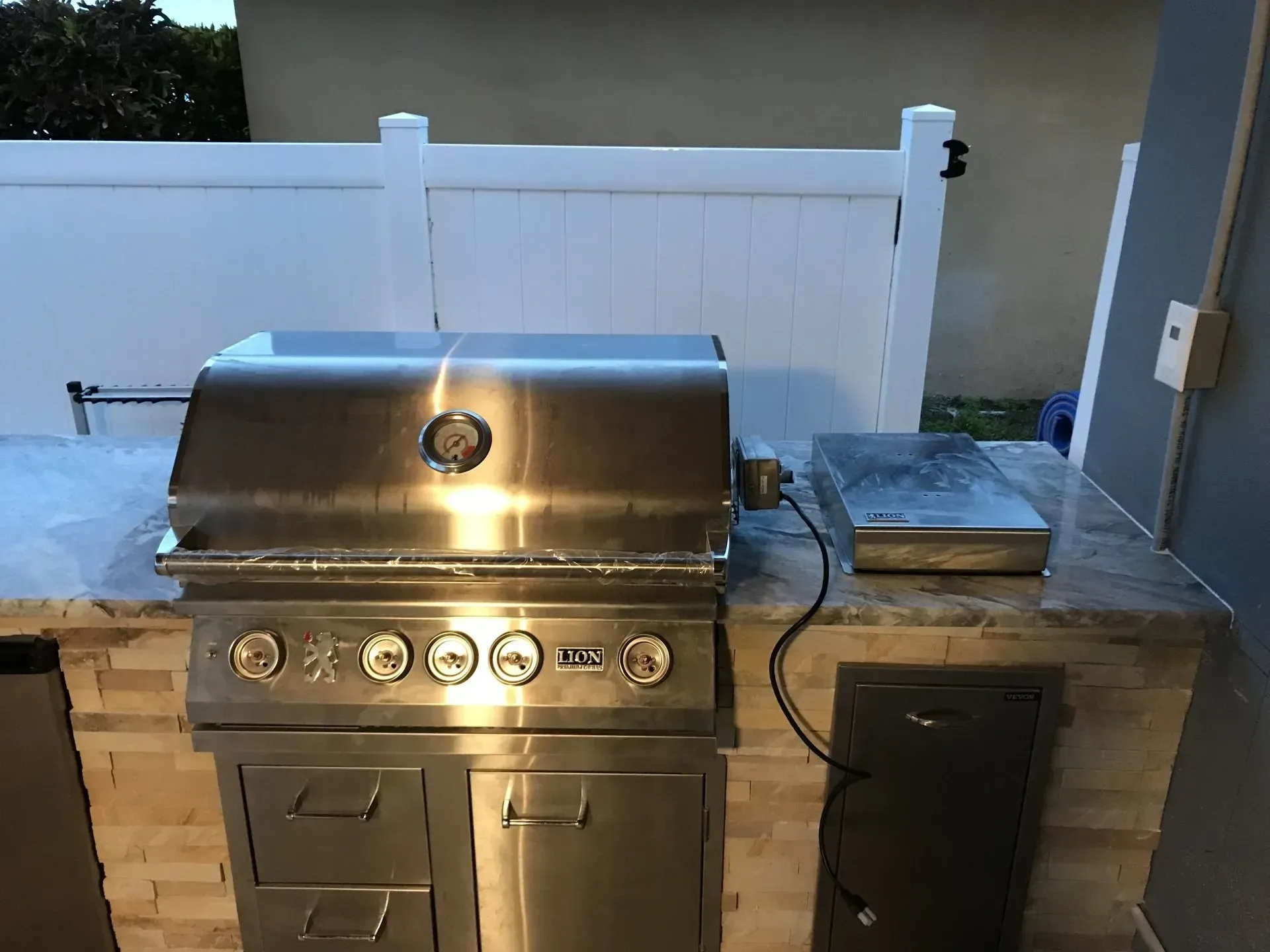 Stainless steel gas grill on a patio beside a prep table and black cabinet outdoors