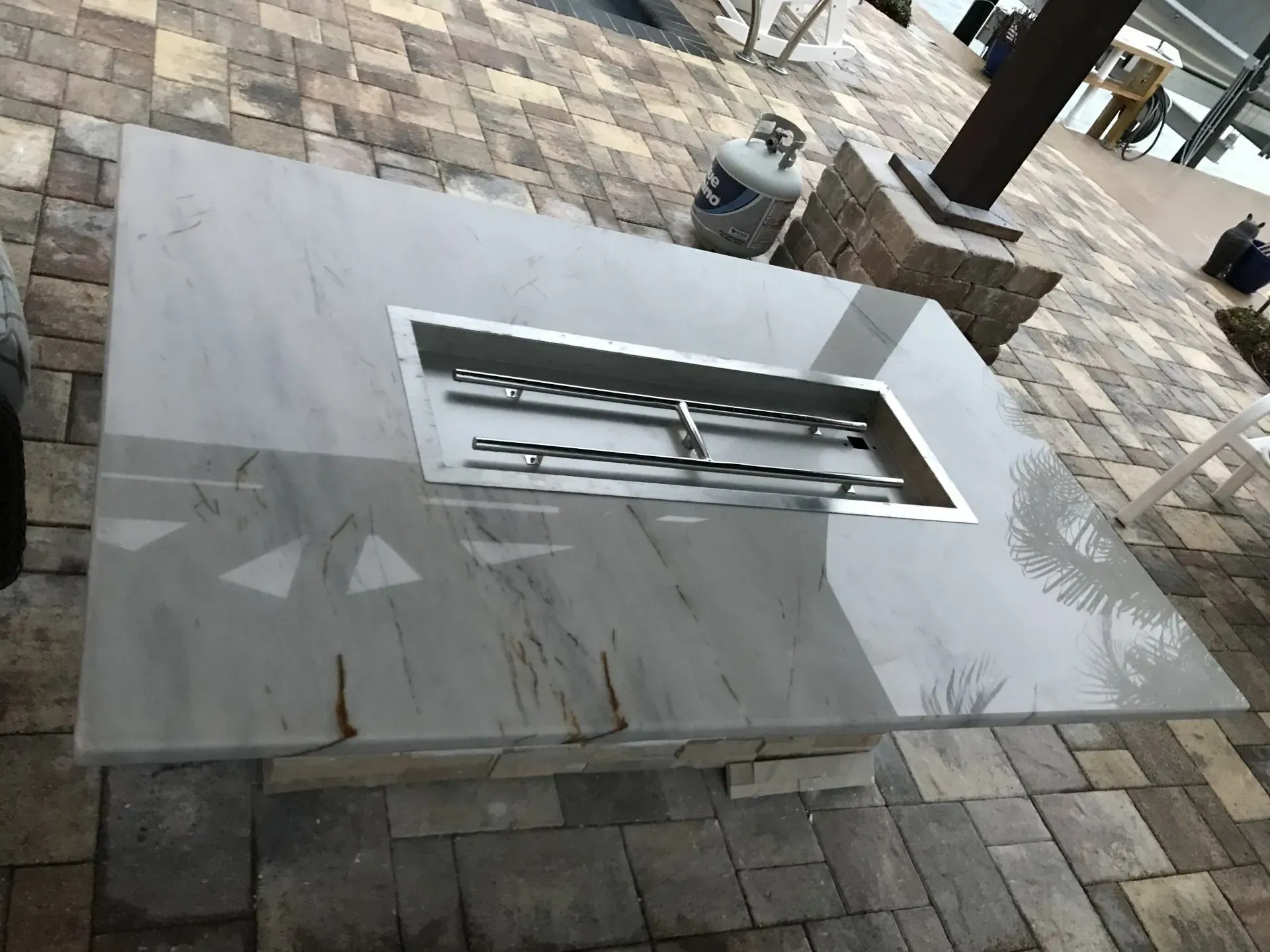 White rectangular outdoor fire pit set into a stone patio with a metal burner insert.