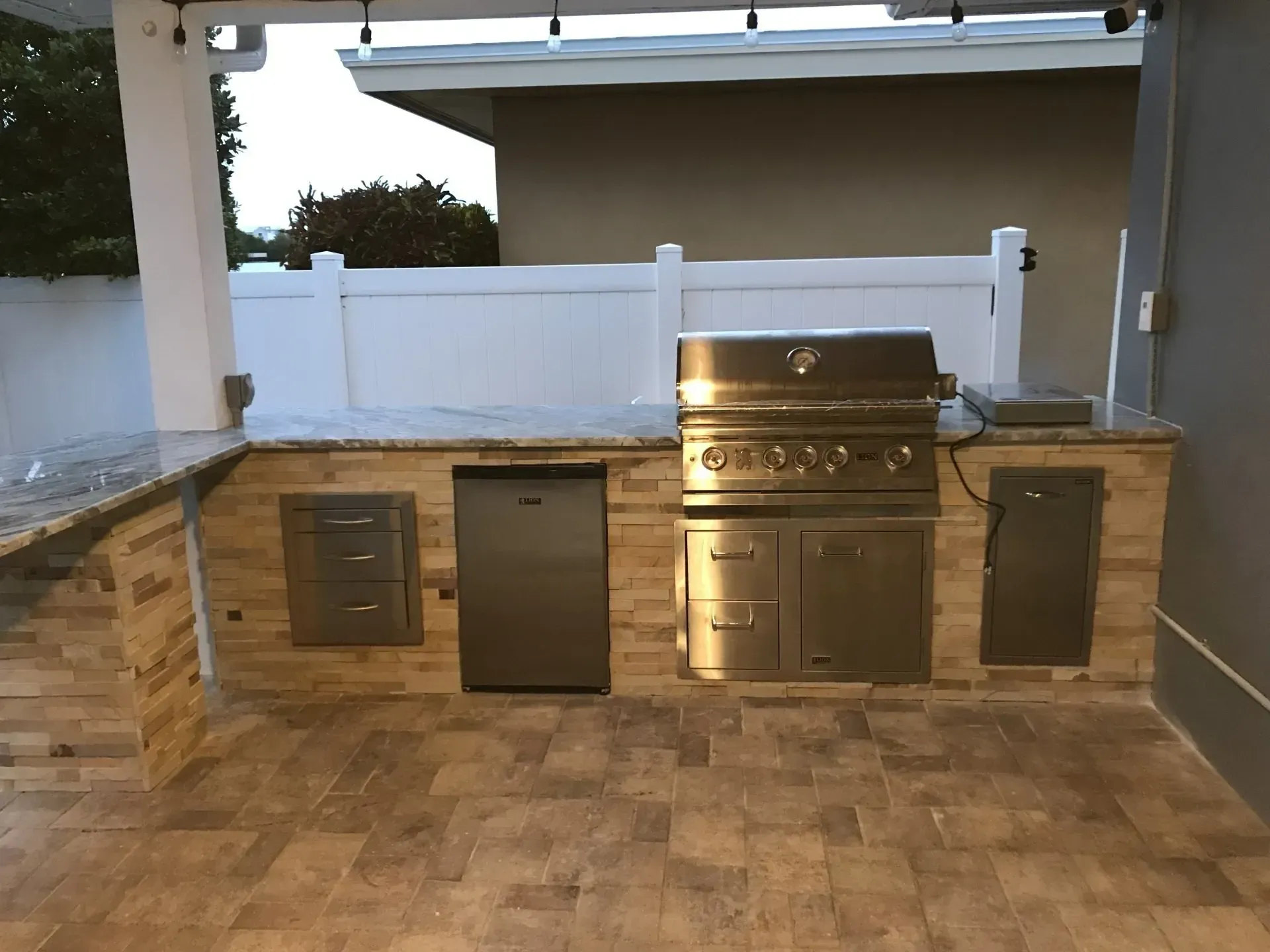 Outdoor patio with stainless steel grill, sink, and cabinets under a covered counter.