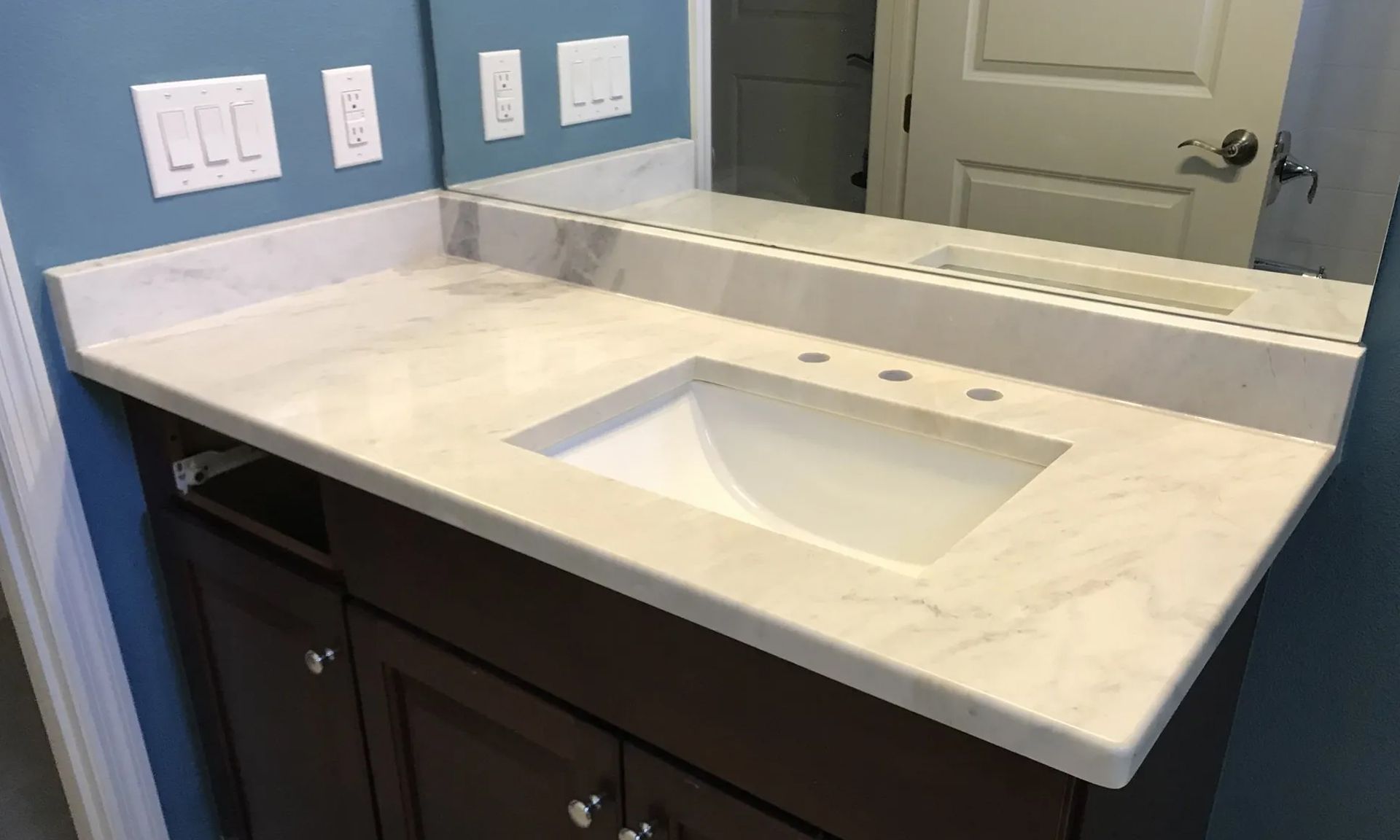 Bathroom vanity with marble countertop and built-in sink, mirror, and dark wood cabinet beneath.